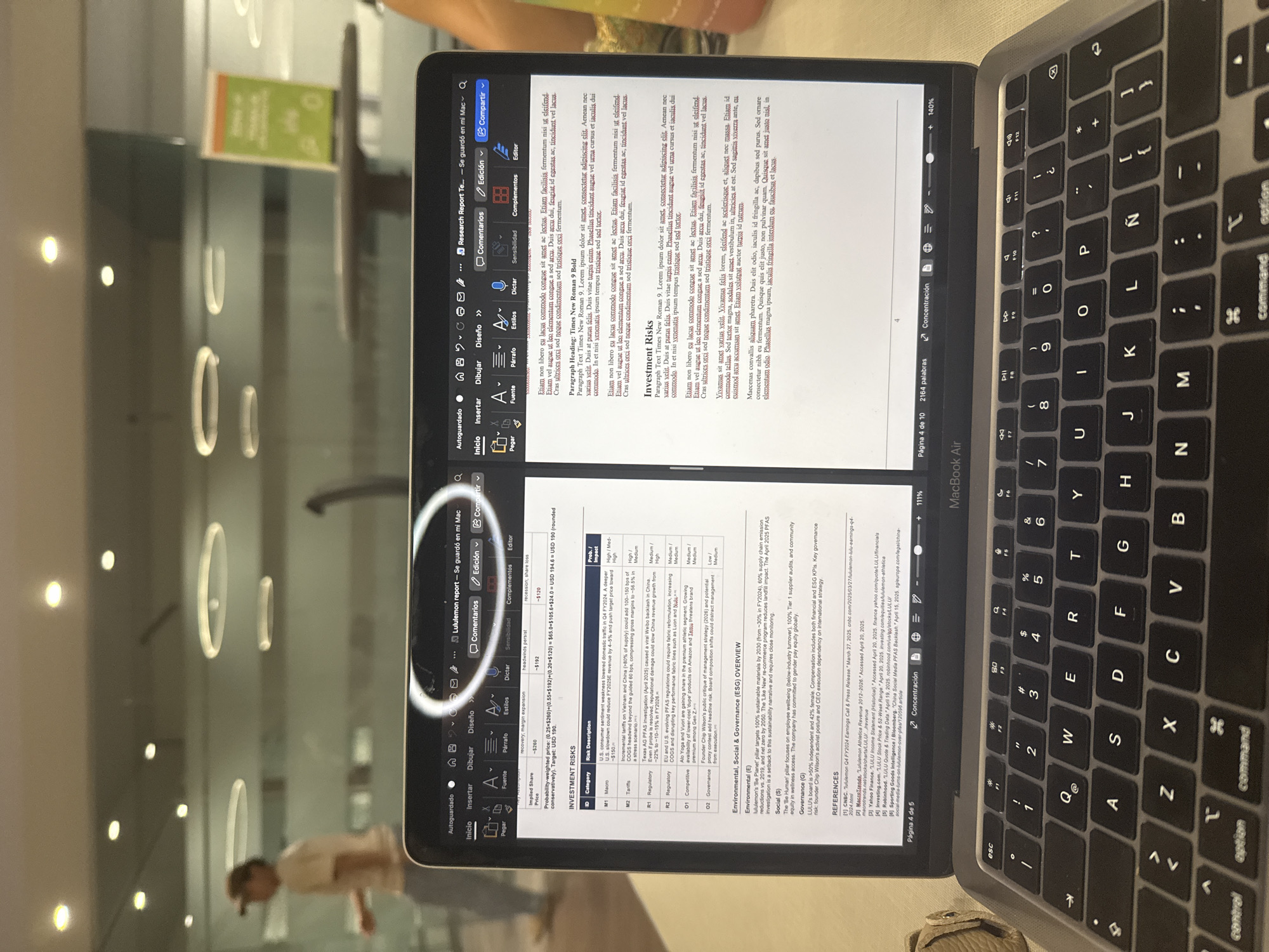 An open MacBook Air laptop is prominently displayed on a surface, likely a table, in an indoor setting. The screen shows a document, which appears to be a "Lululemon report" or "Research Report," open in a word processing application with menus in Spanish, such as "Autoguardado" (Autosaved), "Inicio" (Home), "Edición" (Edit), and "Compartir" (Share).
The document's content is visible, focusing on "INVESTMENT RISKS" and an "Environmental, Social & Governance (ESG) OVERVIEW." The "Investment Risks" section includes a table with categories like Macro, Tariffs, Regulatory, Competitive, and Governance, detailing potential risks and their probable impact (e.g., High/Med-High). The ESG section discusses Lululemon's sustainability targets, employee wellbeing, and governance practices, including references to sources like CNBC, Yahoo Finance, and Robinhood. The document shows text like "Página 4 de 10" and "2164 palabras," indicating its length.
In the background, out-of-focus reflections of circular and elongated lights are visible, suggesting a modern interior with glass or reflective surfaces. A blurred figure of a person is also faintly discernible in the reflections. A hand or arm is seen in the upper right, possibly operating the laptop. The laptop's keyboard features a Spanish layout, identifiable by the "Ñ" key. The setting appears to be a well-lit indoor space in San Andrés Cholula, Mexico, possibly a workspace or public area.