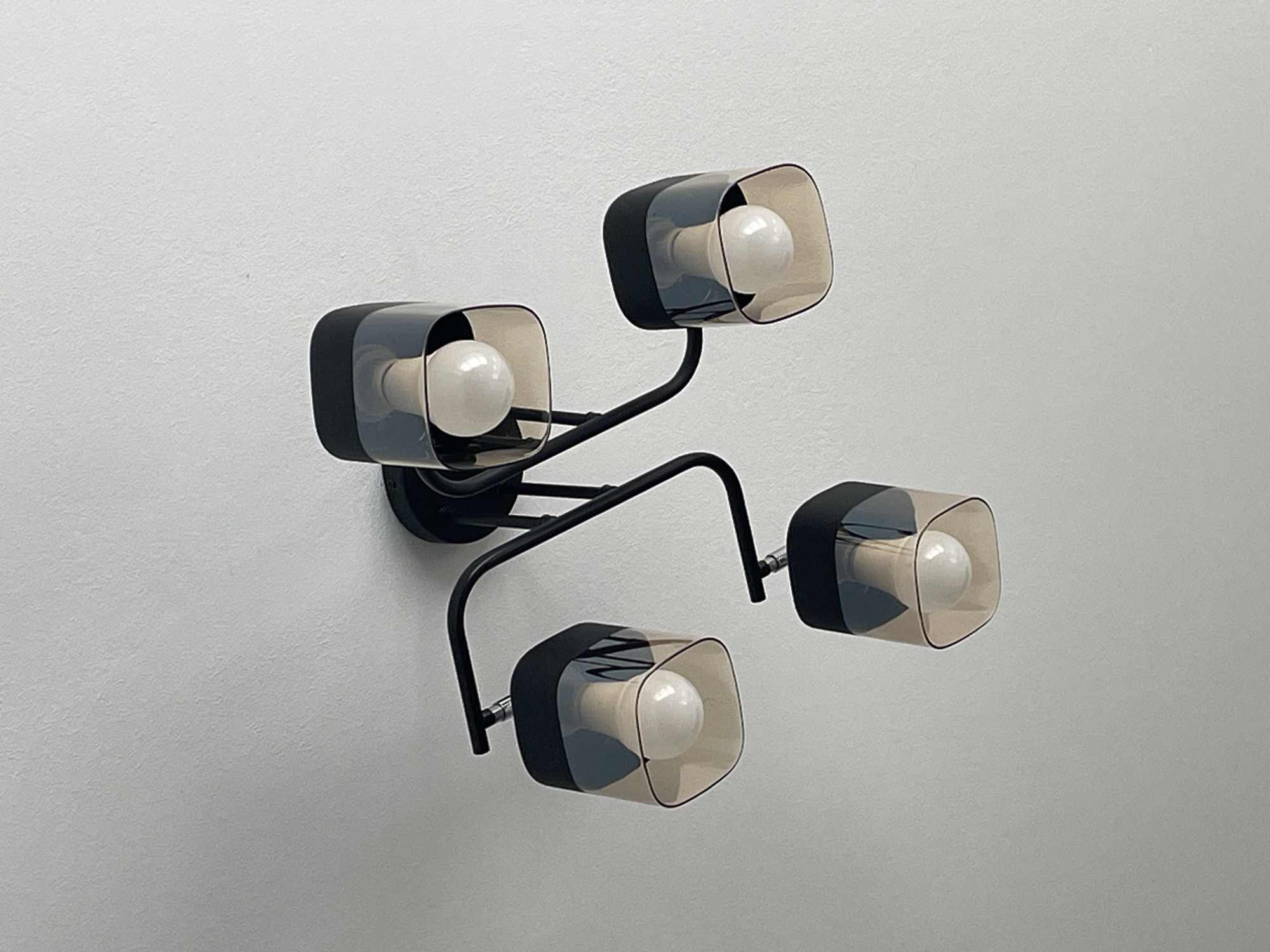 A black, four-bulb modern ceiling light fixture is mounted on a white ceiling. Each bulb is encased in a square-shaped, transparent amber glass shade with a black trim at the top. The fixture has a central black base from which four black arms extend, each supporting a light. The scene is photographed from below. The location is irrelevant to the forensic description.