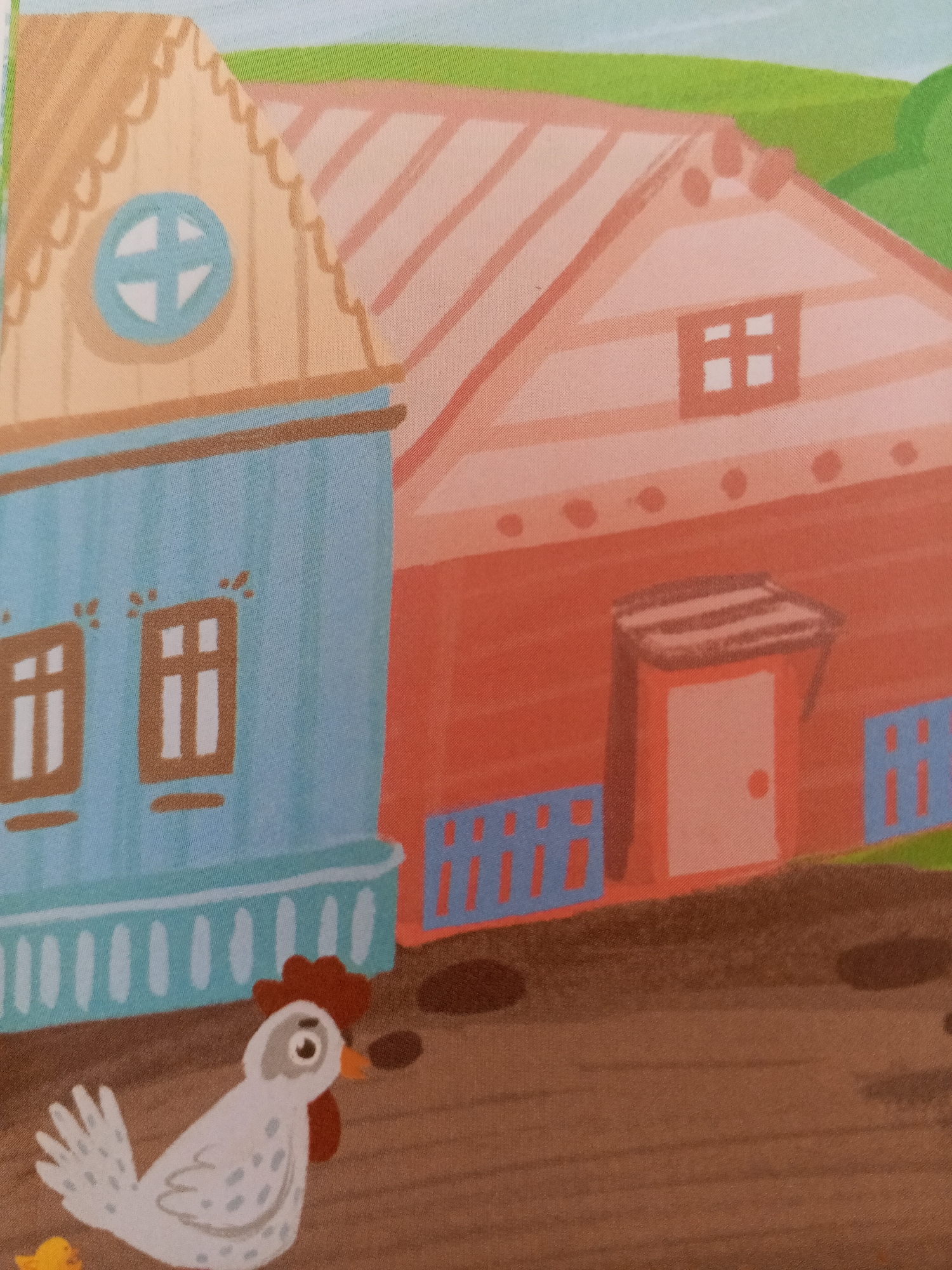 The image depicts a cartoon illustration of a rural scene with two houses and a chicken in the foreground. The house on the left is light blue with two windows, each divided into four panes. It has a light brown roof with decorative scalloped edges and a circular window with a cross-like design. The house on the right is orange-red and has a rectangular window with four panes and a dark gray roof. A dark gray doorway with a light pink door is visible on its front. Both houses have blue picket fences. The ground is brown, and there are some dark brown puddles. In the foreground, a white chicken with grey spots and a red comb is walking towards the viewer. A small yellow chick is partially visible to the left of the chicken. The background shows a green hill and a light blue sky. There is no indication or information within the image to suggest its location in Chistopol, Russia.