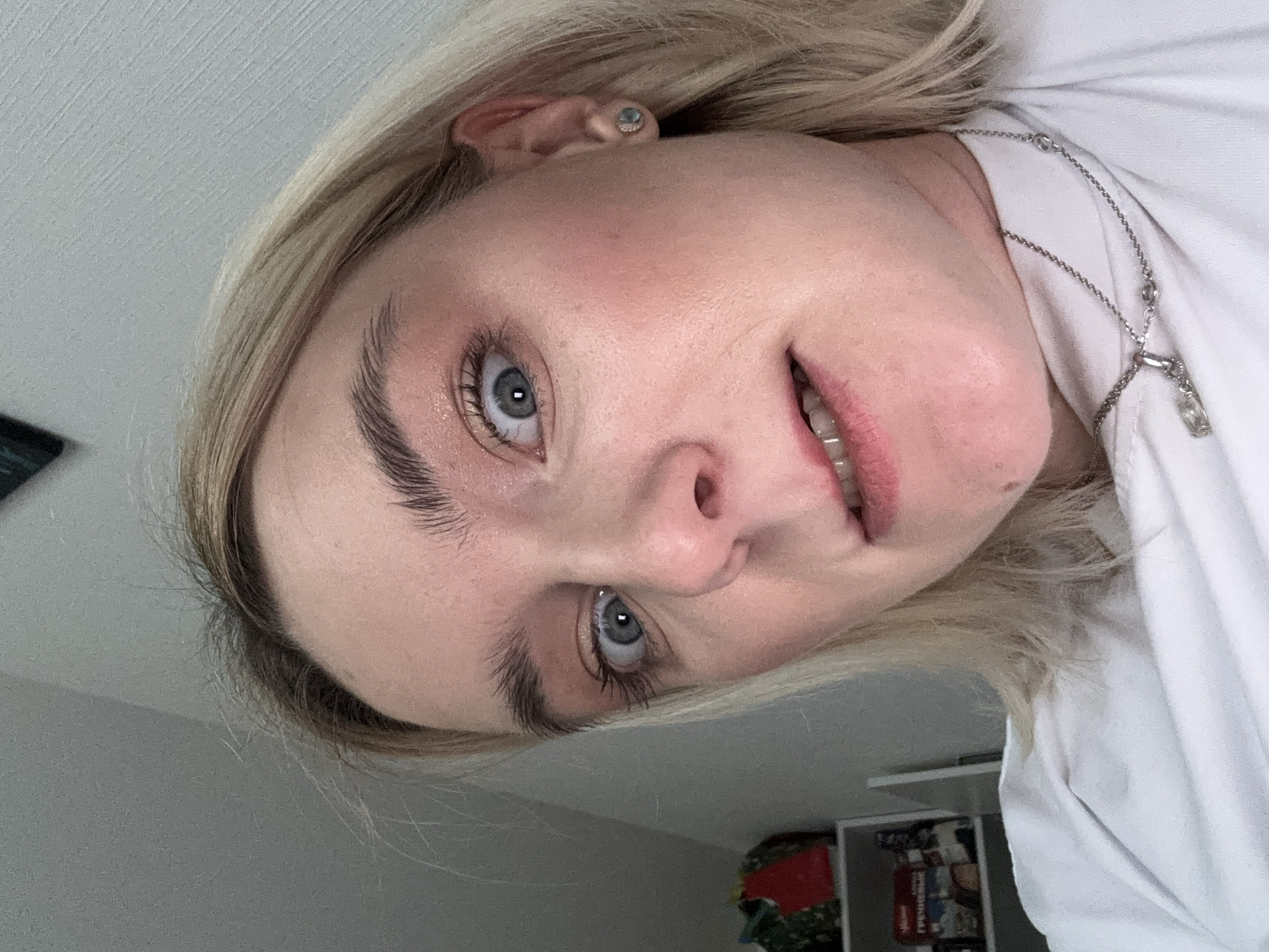 A close-up, angled view of a person with fair skin and light blonde hair. The person has blue eyes, prominent eyebrows, and is wearing a silver necklace. The individual is wearing a white garment. The location is not discernible from the image. There is no information to indicate the city of Vsevolozhsk, Russia.
