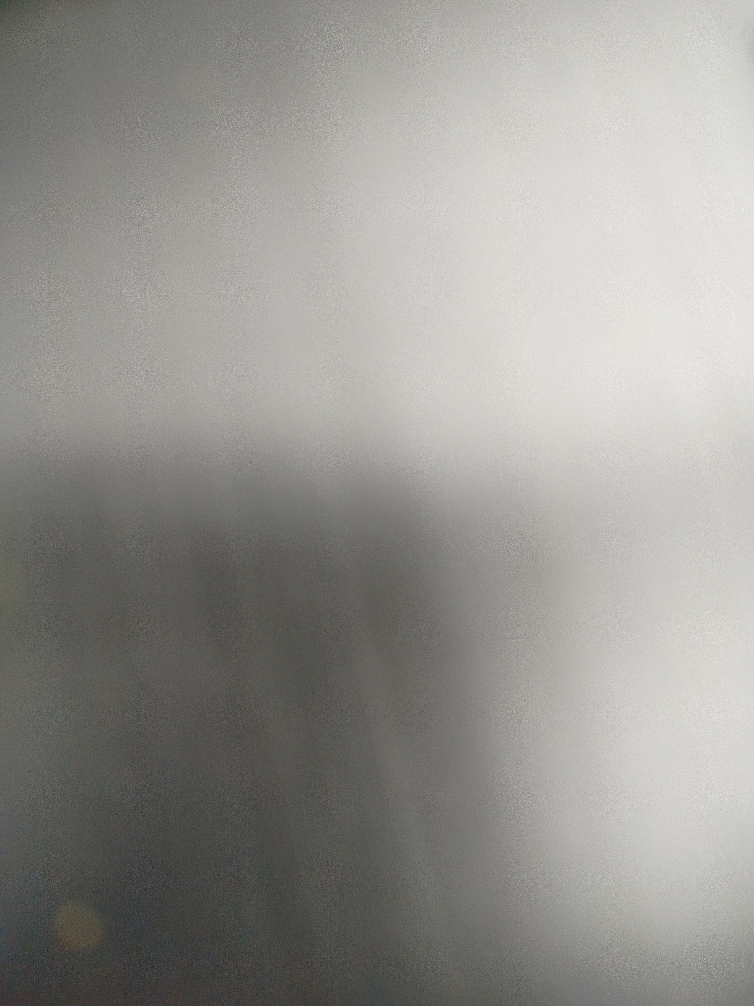 The image is a blurred and indistinct view. The upper portion is lighter in tone, gradually darkening toward the bottom of the frame. There's a subtle transition from a lighter, possibly white or light gray area to a darker, grayer section. At the bottom-left there's a vague lighter spot. The image lacks sharp details, making it impossible to identify specific objects, subjects, or locations including Yerevan, Armenia.