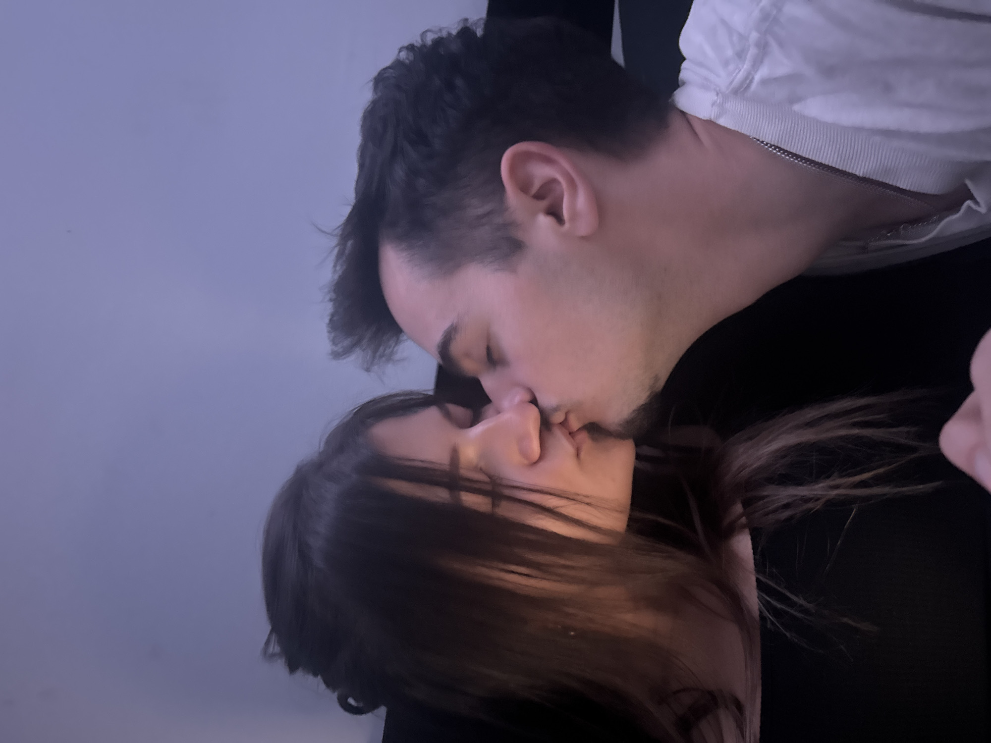 A couple is kissing. The male has dark hair and is wearing a white shirt. The female has long, dark hair. The background is indistinct and does not reveal any information about the location, making it impossible to determine if the photo was taken in Sofia, Bulgaria or elsewhere.