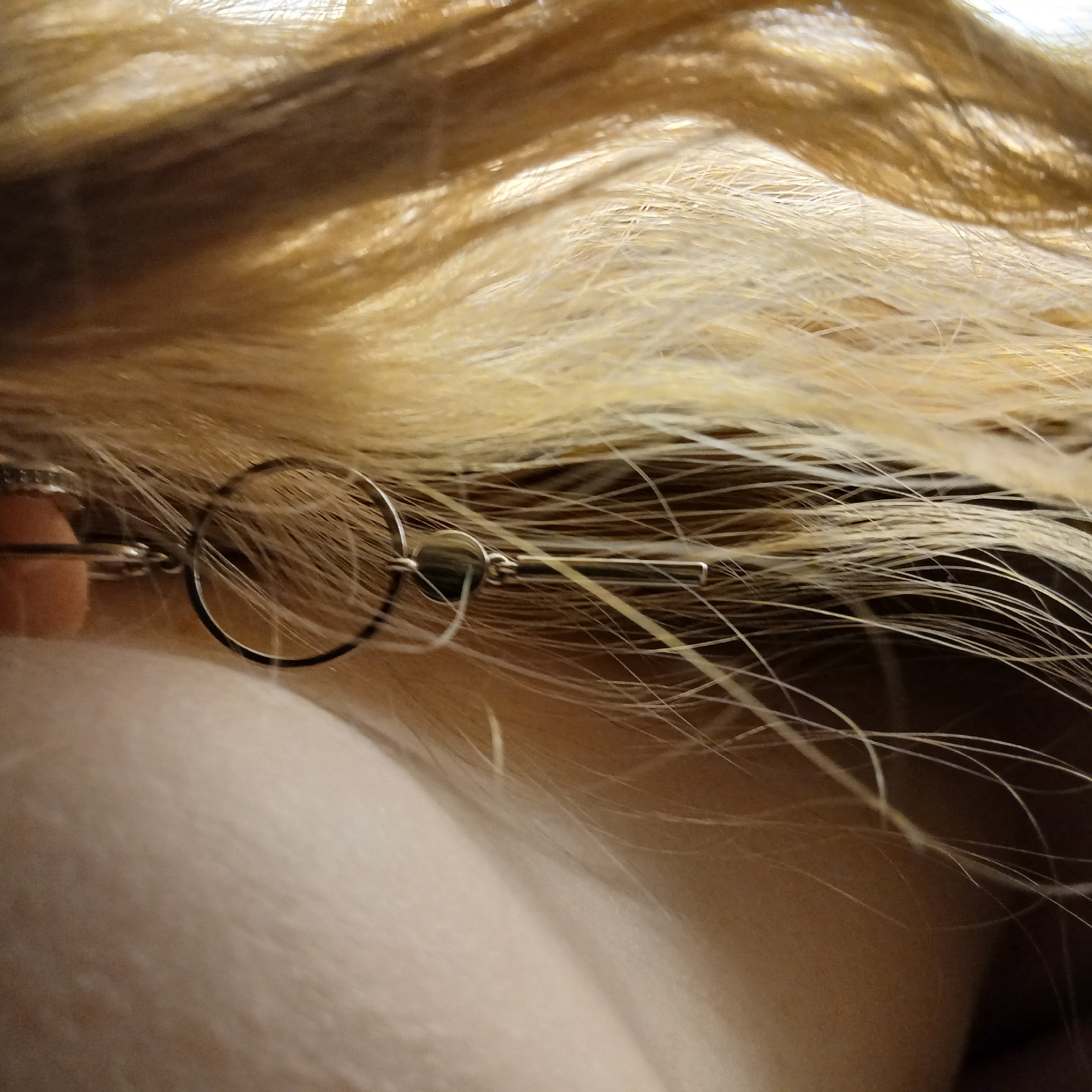 This close-up image features a person's light-colored hair and a metallic accessory. The upper portion of the frame is dominated by flowing blonde or light brown hair, exhibiting individual fine strands that catch the light, creating various shades and textures. Below the hair, a segment of smooth, light-toned skin is visible, likely belonging to a shoulder or neck.
Nestled within the hair, near the skin, is a silver-toned, minimalist accessory. It comprises several connected elements: a prominent circular ring, a smaller, darker disc or bead attached to the ring, and a sleek, elongated rectangular bar extending from the disc. A curved, hook-like component is visible on the far left, suggesting the accessory is either an earring or a hair clip. The metal is reflective, indicating a polished surface.
The lighting is soft, illuminating the hair and accessory, while also creating subtle shadows that give depth to the strands and the contours of the skin. The image is static, with no discernible activity occurring. No text is visible. The context of Yekaterinburg, Russia, is provided, but no specific visual cues within the frame confirm this location or time of day.