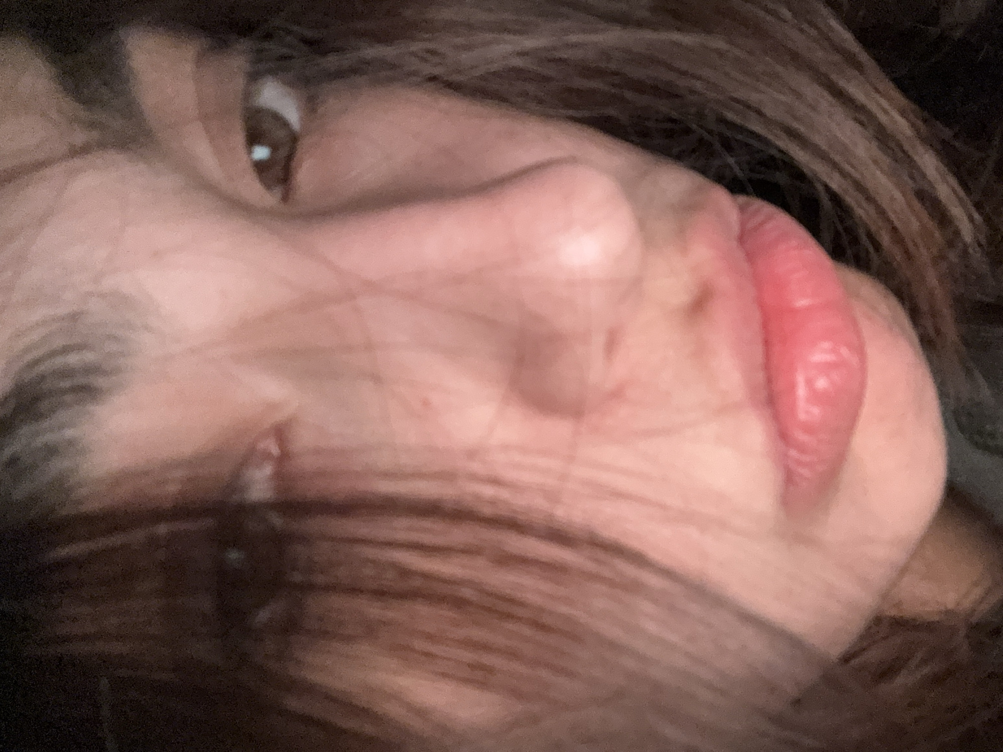 Close-up of a person's face, tilted slightly to the right, with brown hair partially obscuring the view. The person's eye is brown, their skin is light-toned, and their lips are pink and plump. The background is dark and out of focus. No indication of location in Puerto Marqués, Mexico, or further context.