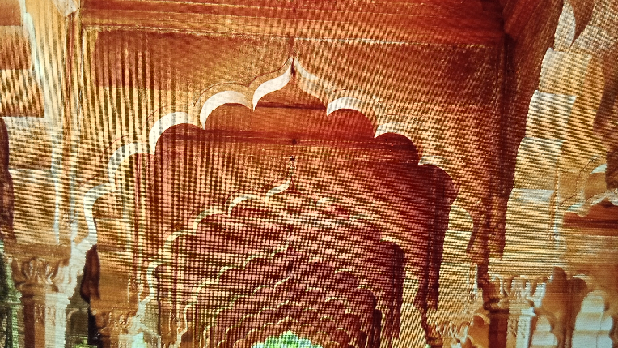 The image shows an architectural detail of multiple arched openings in a warm, reddish-brown building. The arches are layered, with smaller arches nested within larger ones, creating a sense of depth and repeating patterns. The material appears to be stone or stucco, with textured surfaces. Some columns are visible on the sides, adorned with decorative carvings. The lighting suggests an interior or covered walkway, with shadows defining the architectural features. There are no people or animals visible in the frame. The overall impression is one of ornate historical architecture. There is no visible indication or information within the image that links it to Pelanjau Jaya, Indonesia.