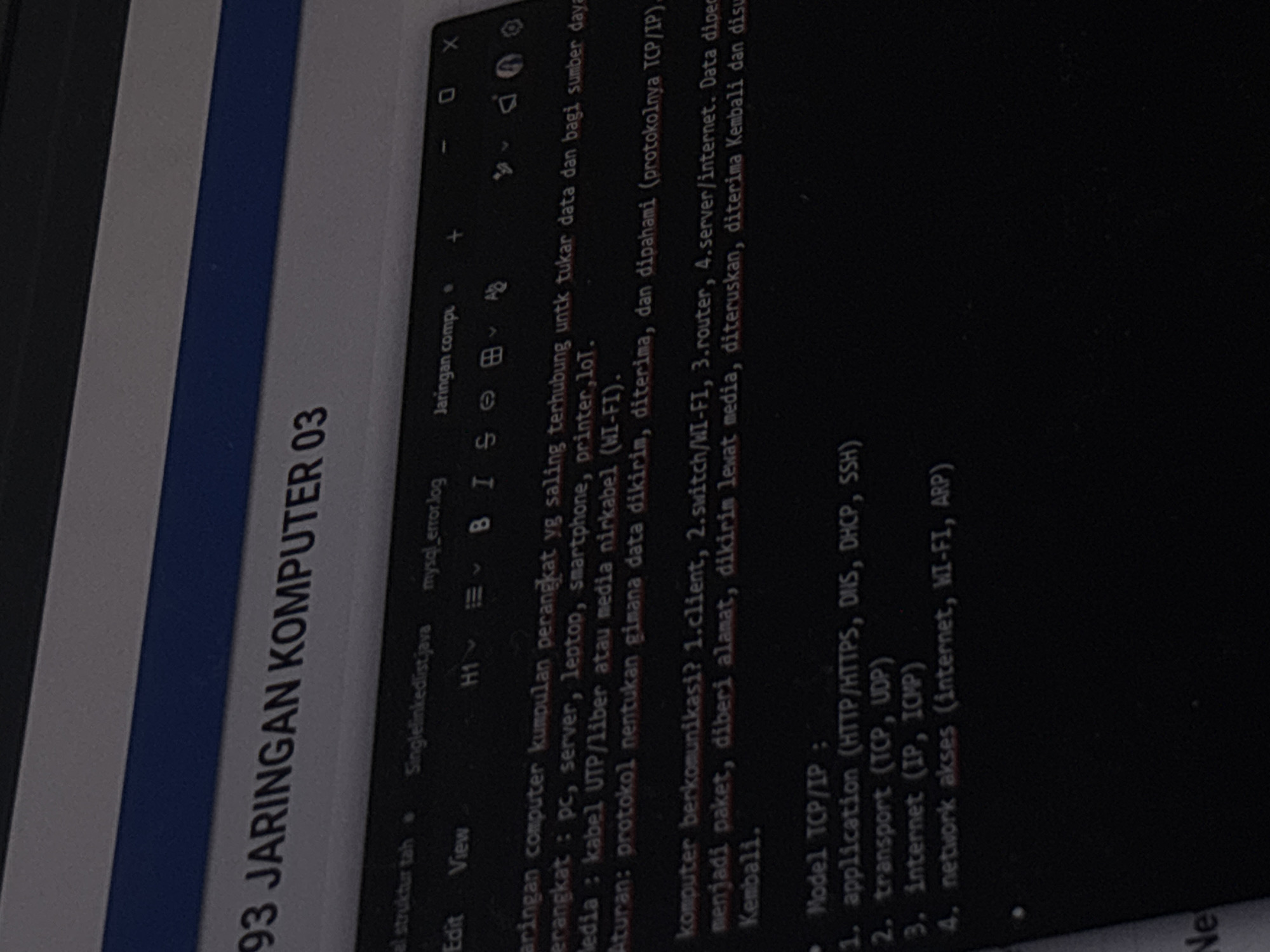 The image shows a close-up of a laptop screen displaying text content, likely from a document or code editor. The text appears to be in Indonesian and discusses computer networking concepts. The top portion of the image displays a blue band, possibly part of the laptop's casing or a banner on the screen. Below this, the text "93 JARINGAN KOMPUTER 03" is prominently displayed, indicating a title or chapter related to computer networks.
The main body of the image shows text in a dark mode interface, with white or light-colored text against a black background. Several lines of text are visible, including:
* "el struktur tah"
* "Singlelinkedlist.java mysql_error.log"
* "Jaringan compl"
* "Edit View"
* "H1" followed by an icon that looks like a font selection menu.
* "B I S ⌂ ⌂ Ab" which seem to be formatting options (Bold, Italic, etc.).
* "aringan computer kumpulan perangkat yg saling terhubung untk tukar data dan bagi sumber daya."
* "perangkat : pc, server, laptop, smartphone, printer,IoT."
* "edia : kabel UTP/liber atau media nirkabel (WI-FI)."
* "Aturan: protokol nentukan gimana data dikirim, diterima, dan dipahami (protokolnya TCP/IP)."
* "komputer berkomunikasi? 1.client, 2.switch/WI-FI, 3.router, 4.server/internet. Data diper"
* "menjadi paket, diberi alamat, dikirim lewat media, diteruskan, diterima Kembali dan disu"
* "Kembali."
* "Model TCP/IP:"
* "1. application (HTTP/HTTPS, DNS, DHCP, SSH)"
* "2. transport (TCP, UDP)"
* "3. internet (IP, ICMP)"
* "4. network akses (internet, WI-FI, ARP)"
The image itself is an indoor shot, likely taken at night or in a dimly lit room, as the screen is the primary light source. There are no visible people or specific environmental details that would suggest a location in Semarang, Indonesia. The scene is focused on the digital content displayed on the laptop screen.