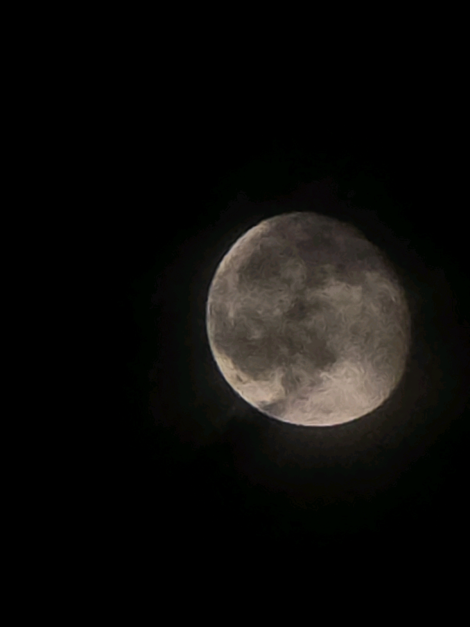 The image shows a close-up, slightly blurry view of the moon against a black night sky. The moon is illuminated and displays visible surface features, appearing as a textured, grayish-white sphere. There are no other celestial bodies or atmospheric phenomena visible. The setting is not specified to be within the city of Shulavery, Georgia. The image is devoid of people, objects, actions, interactions, or any discernible urban environment.