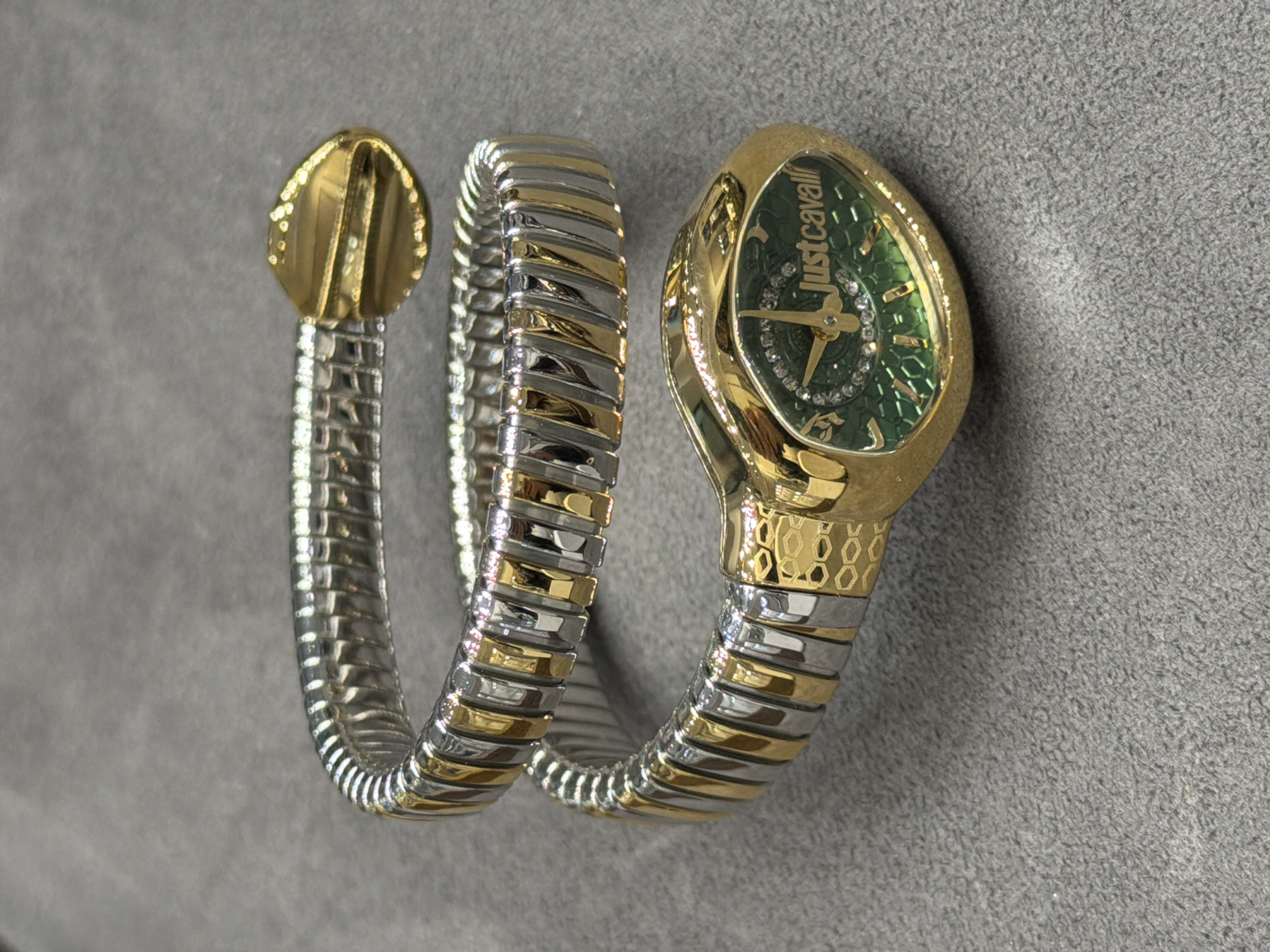 The image shows a gold and silver "Just Cavalli" snake bracelet watch. The watch is coiled on a gray surface. The face of the watch is green, and the bracelet is composed of alternating silver and gold links, with the head of the snake rendered in gold. The watch is not being worn, and there are no other visible objects or people. The location in Yerevan, Armenia, cannot be determined from the image.