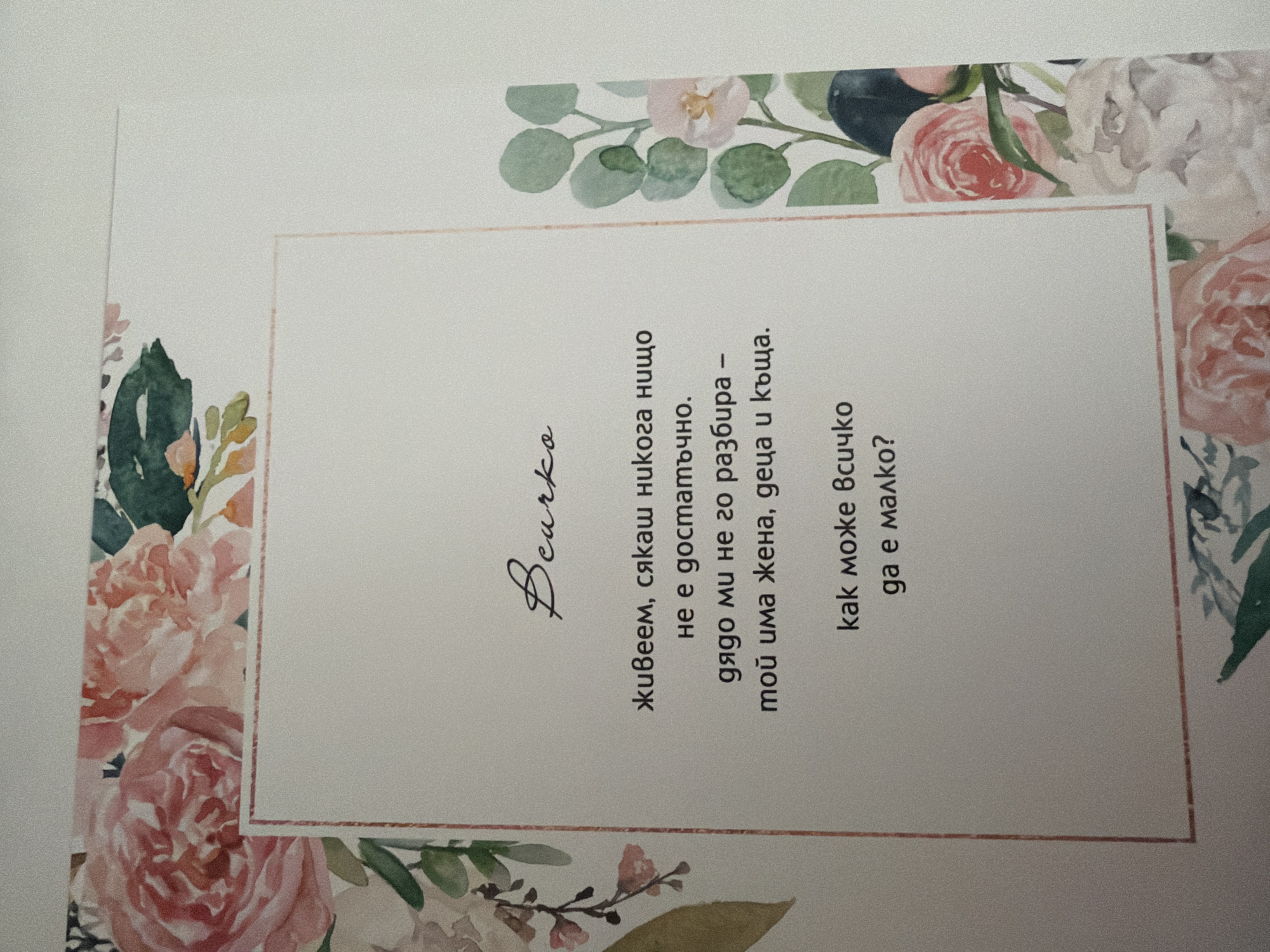 The image shows a close-up of a printed page with floral watercolor decorations around the edges. In the center of the page, there is a handwritten signature in cursive that reads "Bourke." Below the signature, there is a short poem in Bulgarian, printed in a serif font. The text is contained within a light pink border. The background of the page is white, and the overall aesthetic is delicate and artistic. The image does not contain any information about the city of Pazardzhik, Bulgaria, or any people, subjects, objects, actions, or interactions that would place it in a specific city or context.