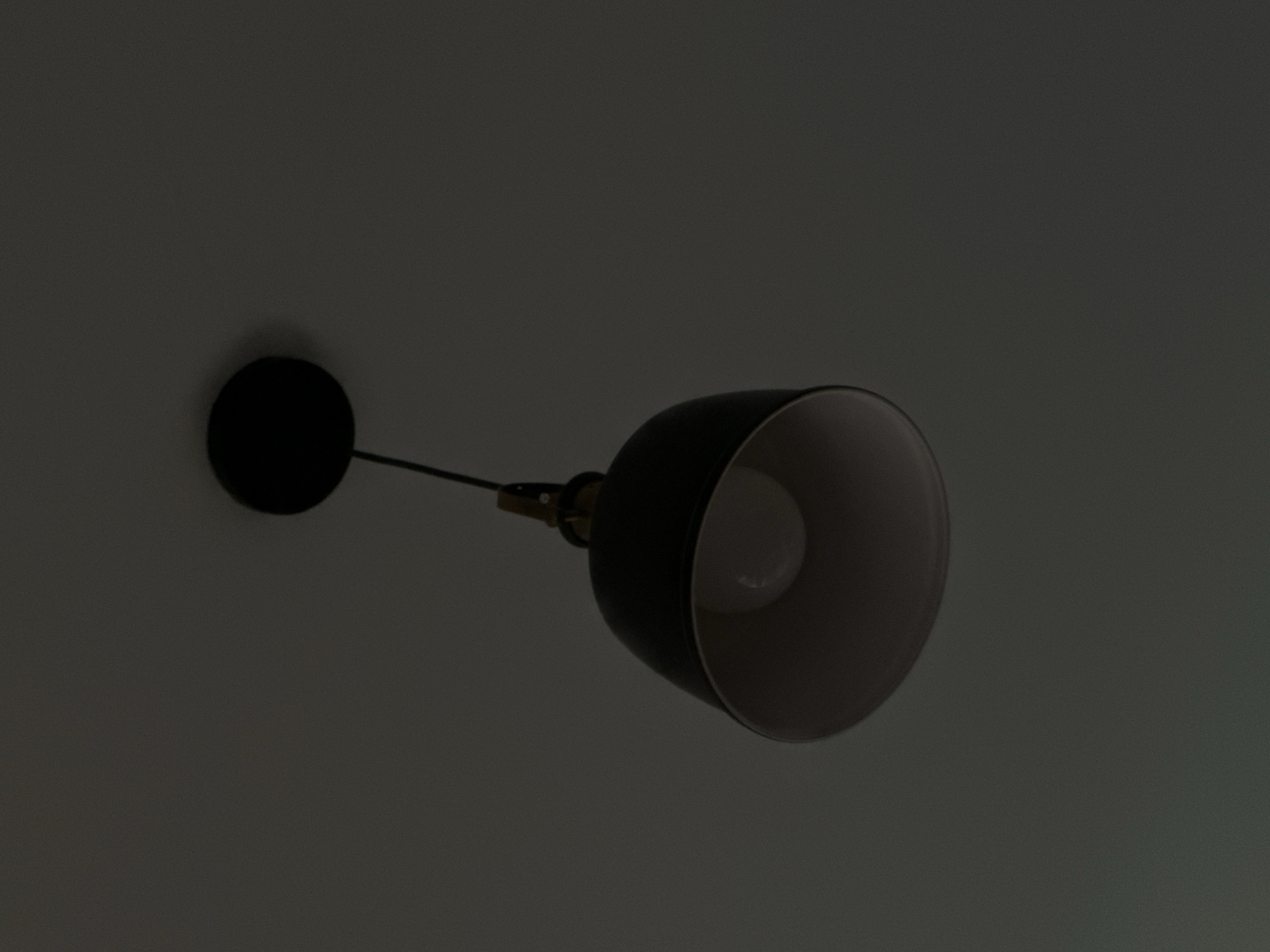 An indoor ceiling light fixture hangs from a dark ceiling. The fixture consists of a black, dome-shaped lampshade with a lighter interior. A visible light bulb is inside the lampshade. The image is dark and the background is a solid, dark gray color. There is no indication of a specific city, including Georgiyevsk, Russia.