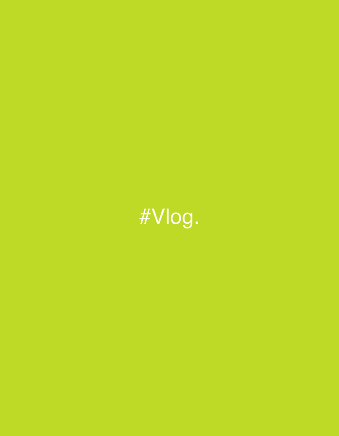 The image displays a uniform lime-green background. Centered on this background is the white text '#Vlog.'