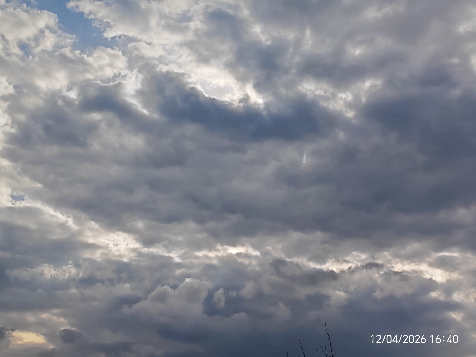The image shows a cloudy sky with the date and time "12/04/2026 16:40" displayed in the bottom right corner. Some gaps in the clouds reveal patches of blue sky. The location is identified as Unknown, Unknown.
