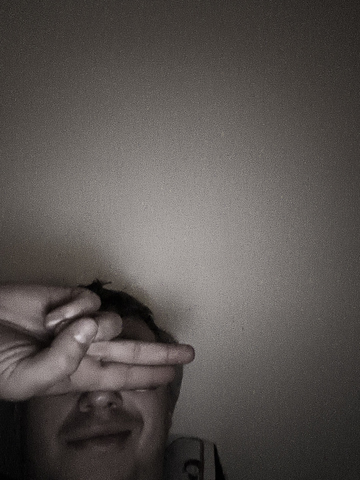 A monochrome, grainy image shows a person covering their eyes with their hand. The bottom half of their face is visible, including the nose and mouth. The background is a plain, undifferentiated wall. There is no indication of Nowy Tomyśl, Poland, in the image.