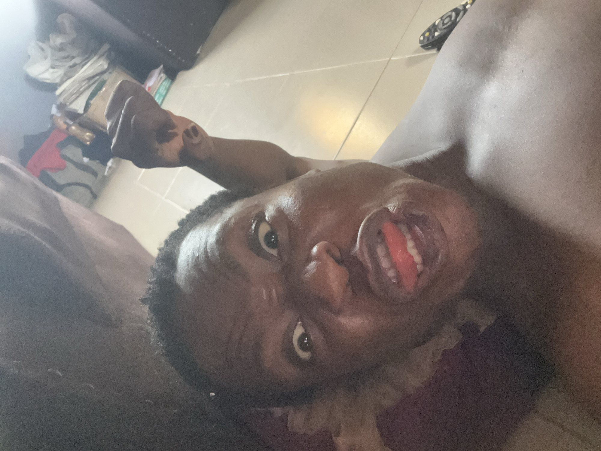 A person is lying down, looking up at the camera. The person's mouth is open, revealing their tongue. The person's fist is clenched in the background. The location is a room with light-colored tile flooring. The city is Unknown, Unknown.