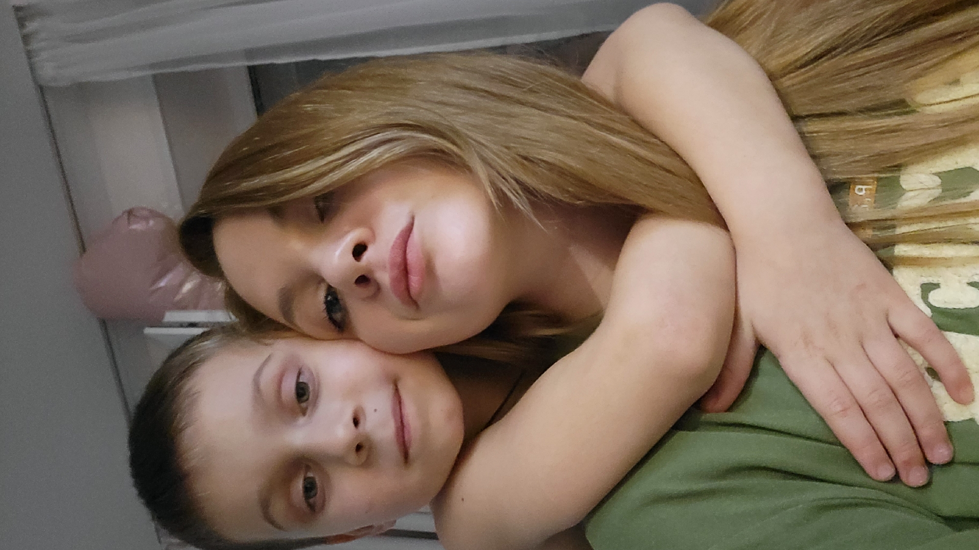 Two people are posing for a photo. The individual in the foreground appears to be a child. The individual behind the child is likely a young adult or teenager with long brown hair. They are embracing each other, and both are looking towards the camera with soft smiles. The background is indistinct, with a glimpse of what might be a balloon. Given the request to include the location in Chaikovsky, Russia, it is presumed that this photograph was taken somewhere in this city. The subjects are likely related, possibly siblings or a parent and child. There are no immediate signs of any illegal activity.