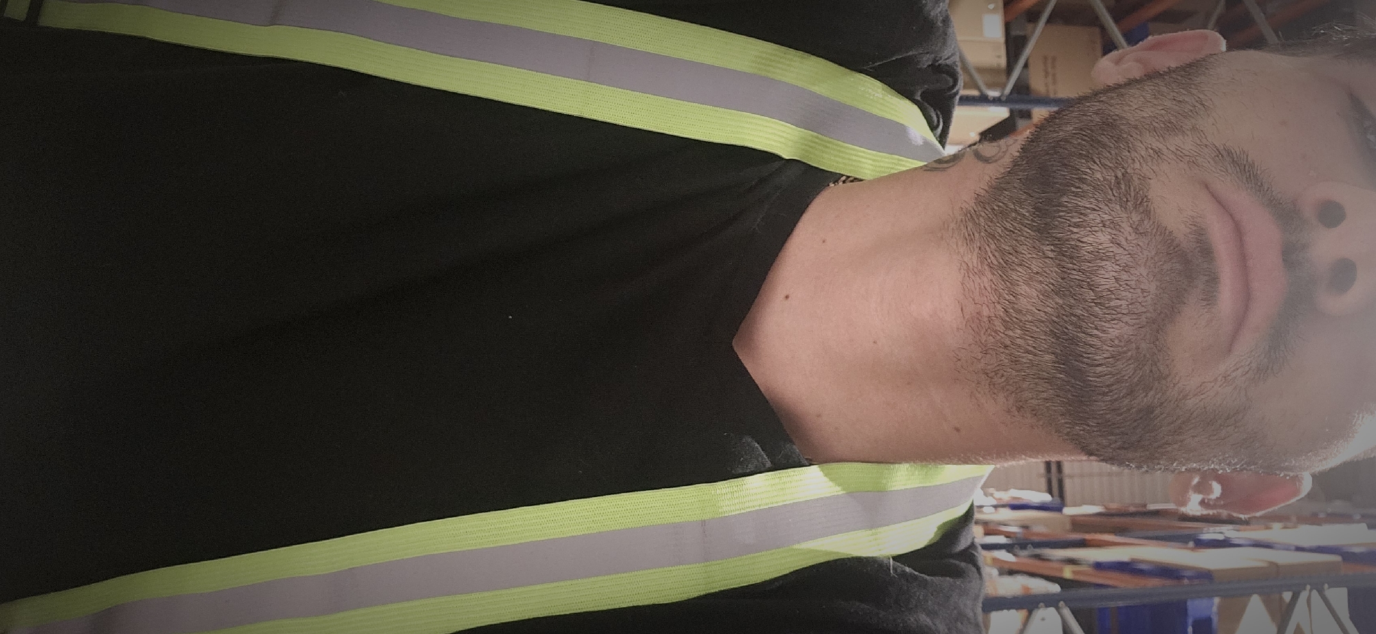 A man with dark hair and a beard is wearing a black shirt with reflective stripes. He appears to be standing in a warehouse. The location in the city of Plovdiv, Bulgaria, is not discernible from the image.