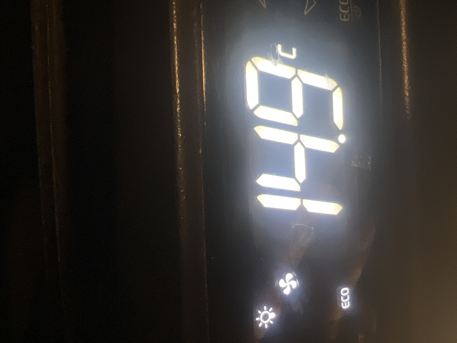 A digital display shows a temperature of 64 degrees Celsius. Below the temperature reading are icons indicating fan speed, sunlight, and eco mode. The display is set against a dark background. The lighting is bright and highlights the numbers and icons. The overall image is slightly tilted.