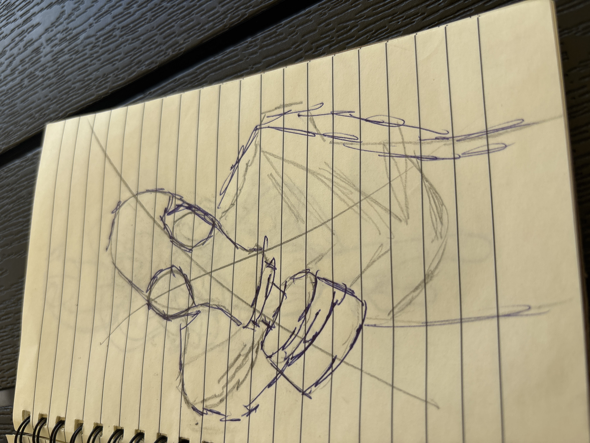 A sketch in progress on lined notebook paper depicts a stylized figure wearing a gas mask and holding a cylindrical object. The drawing is done in blue ink and graphite. The background of the image shows a dark, textured surface, likely a table. The sketch is positioned on the left side of the notebook page, with the spiral binding visible on the left edge. The image is a close-up of the notebook and does not depict any identifiable location in Karviná, Czechia.