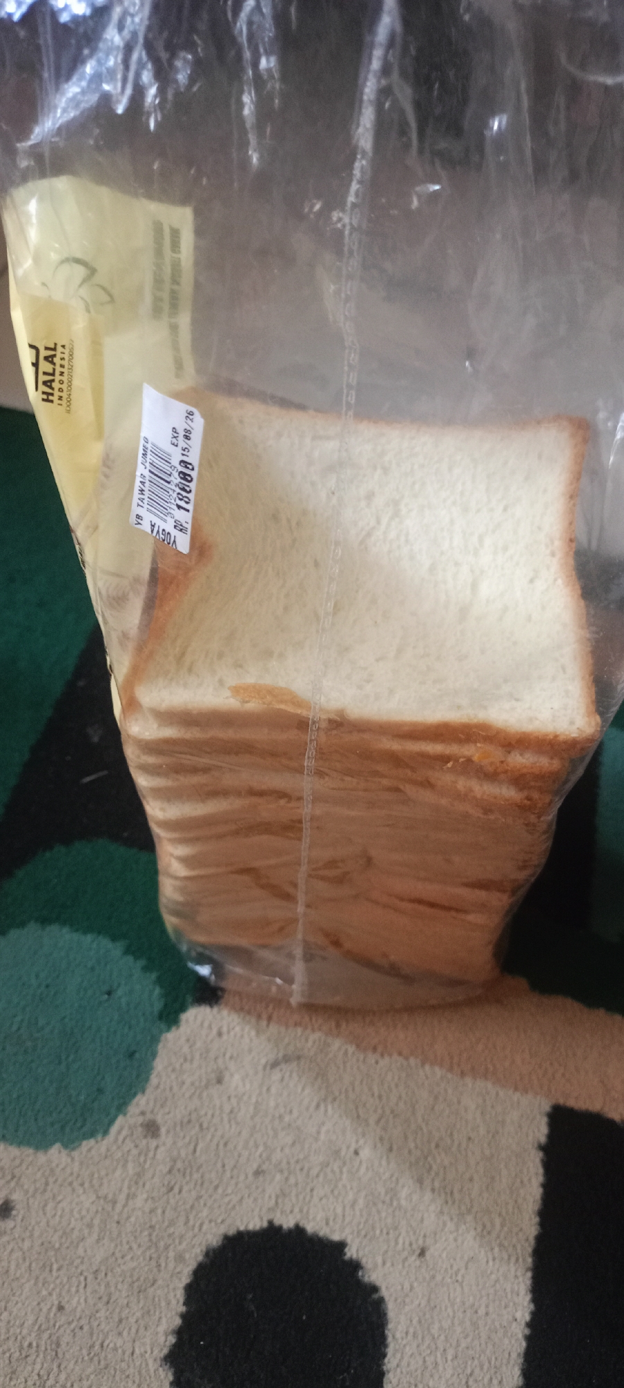 The image shows a loaf of white bread packaged in clear plastic. A label is attached to the plastic, displaying information in Indonesian. The bread is stacked with its slices facing the viewer. The background suggests an indoor setting with a patterned rug. The location of Margahayu Selatan, Indonesia is not visible in the image.