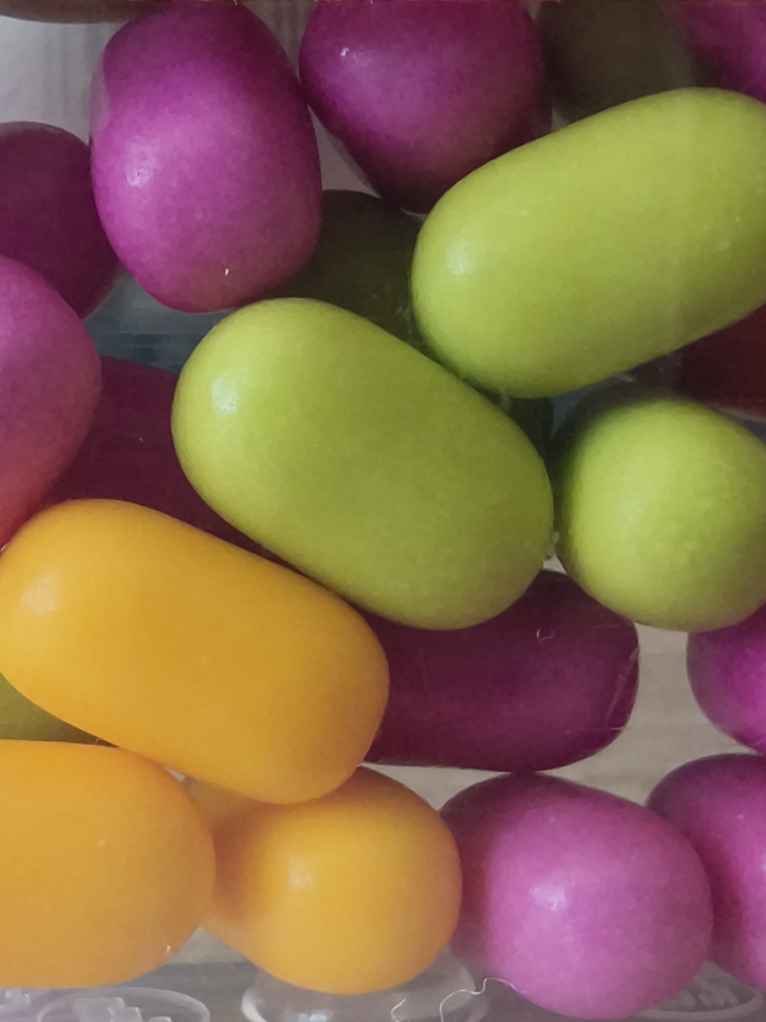 The image shows a close-up of colorful, capsule-shaped candies in shades of purple, green, and yellow. The candies appear to be in a clear container. There is no indication of a location in Kryvyi Rih, Ukraine, or any people, subjects, or actions.
