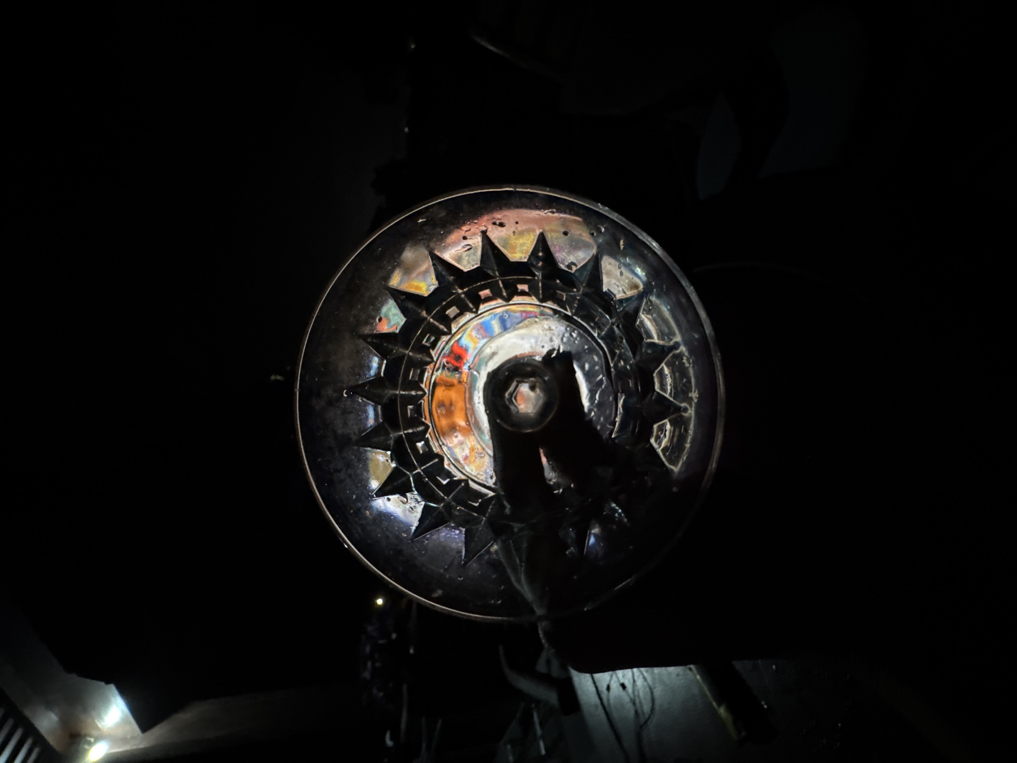The image shows a clear glass with a starburst pattern around its base, seen from below. The glass is likely hand-held, as a darkened hand is visible holding it. The background is dark, with only subtle light reflecting on surfaces beneath the glass. Based on the prompt, the location is in Ungasan, Indonesia. No further specifics about the location or any people involved can be determined from the image.