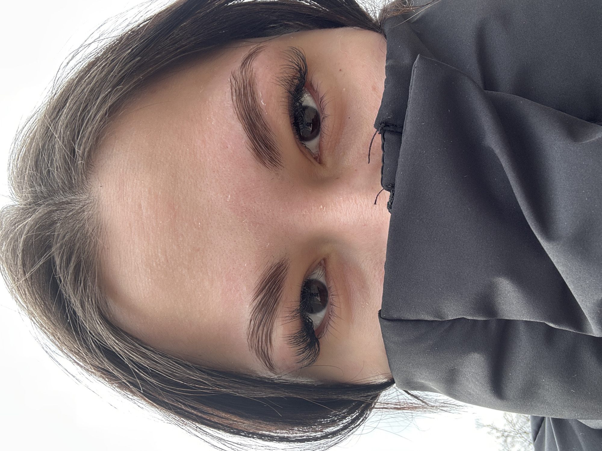 A close-up, tilted portrait features a person's face, primarily focusing on their eyes and eyebrows. The person has dark hair and fair skin. Their eyebrows are well-groomed and defined, and they have long, dark eyelashes, appearing to be extensions. The right side of their face is partially obscured by a dark, possibly black, fabric or garment.
Given the prompt mentioned Chaikovsky, Russia, it is assumed that the photo was taken somewhere in the city, but there is no explicit evidence of the location visible in the image.