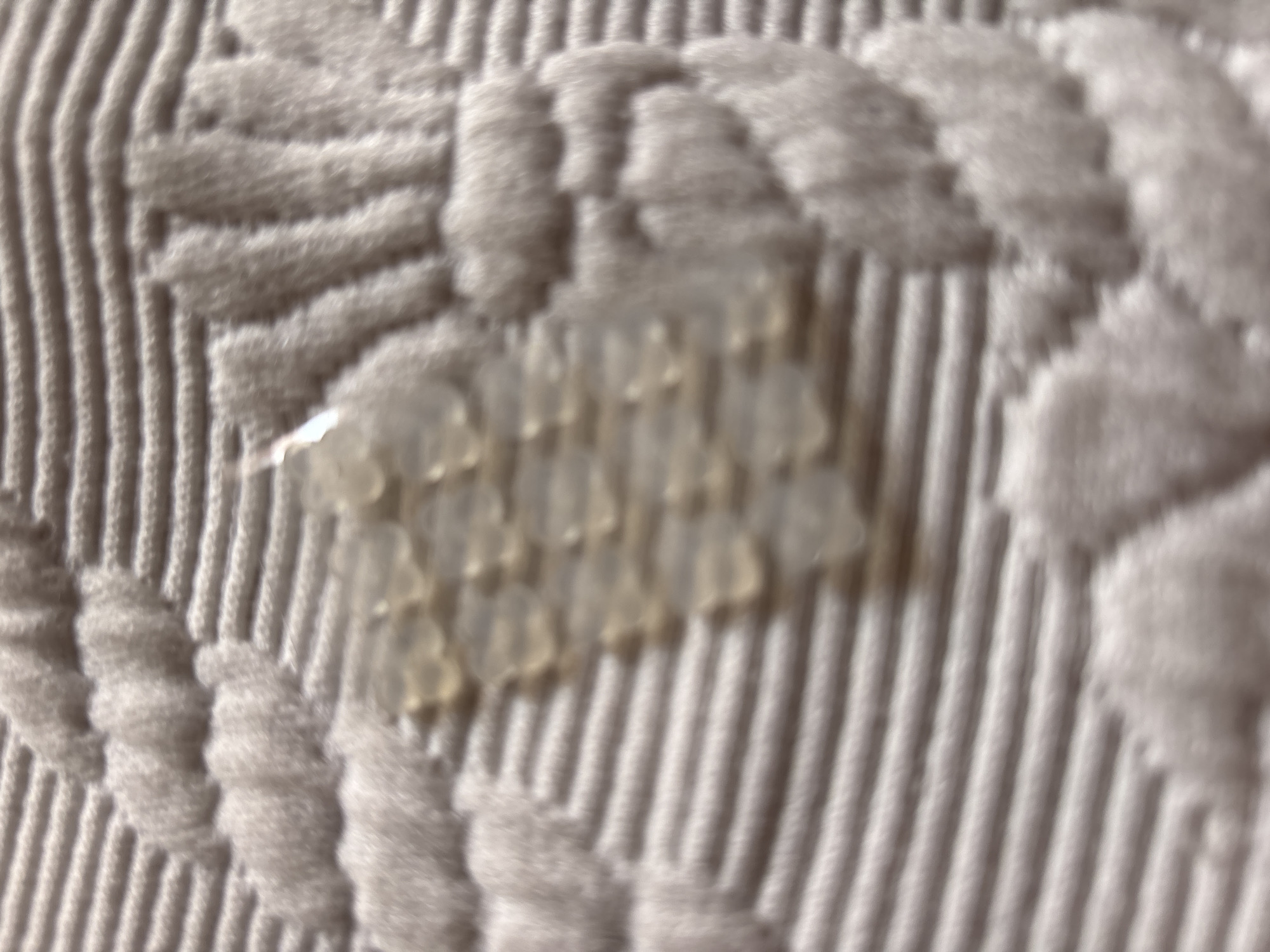 The image is a close-up, out-of-focus shot of a textured fabric with a pattern that resembles rope or braided strands. There is a cluster of small, translucent, gel-like droplets on the fabric. The background is a series of thin, parallel lines. The lighting is soft and diffused, creating a hazy effect. The image does not contain any identifiable landmarks or elements that would allow for its location to be determined within the city of Chernogorsk, Russia, or any other specific location.