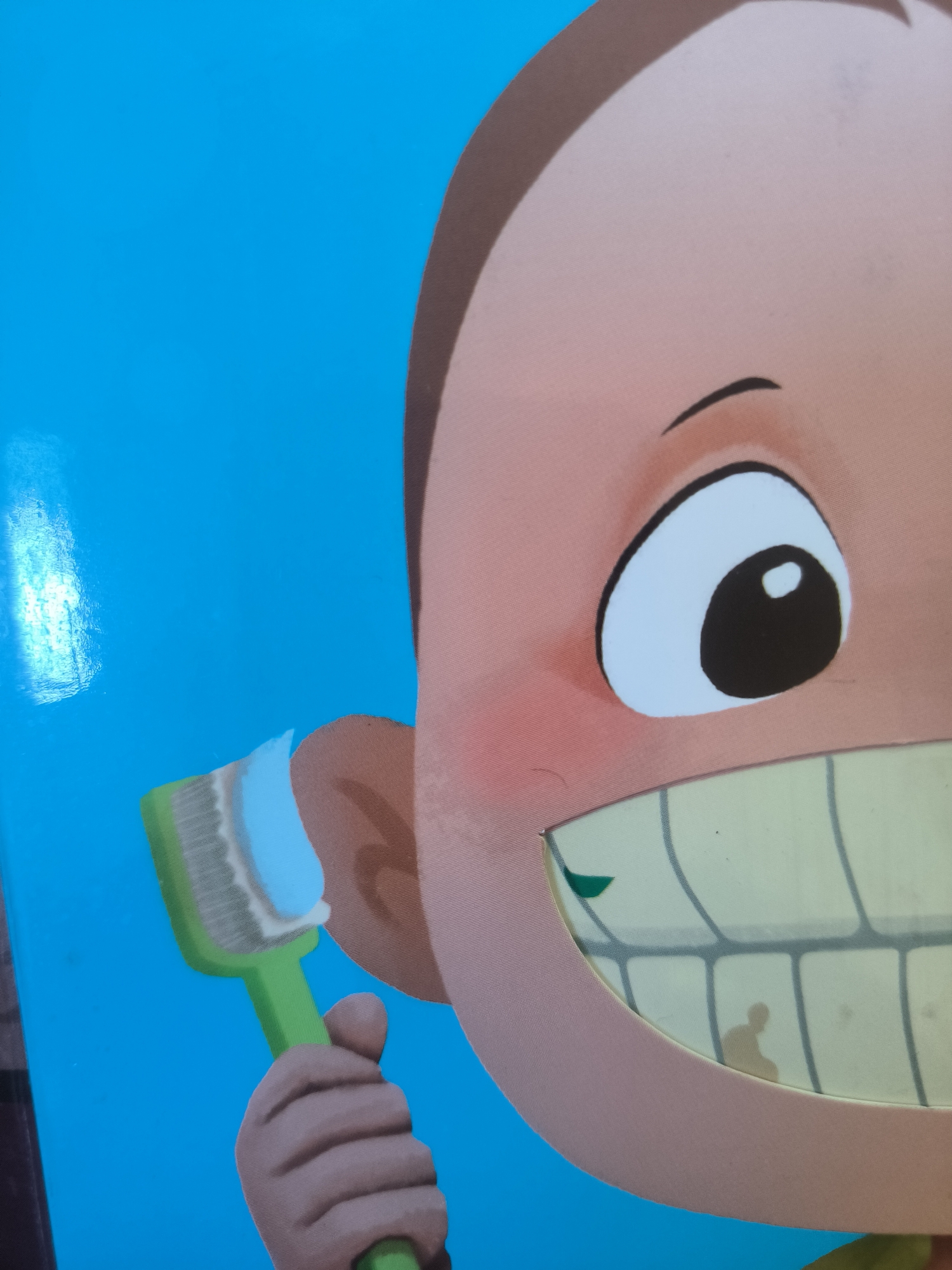 The image is a close-up of an illustration on a blue background. The illustration features part of a cartoon character's face, including an eye, a section of the head with brown hair, and part of a mouth showing teeth. The character is holding a green toothbrush with white toothpaste.
The image does not show any identifiable location. Therefore, it is impossible to determine if this image was taken in the city of Lhokseumawe, Indonesia.