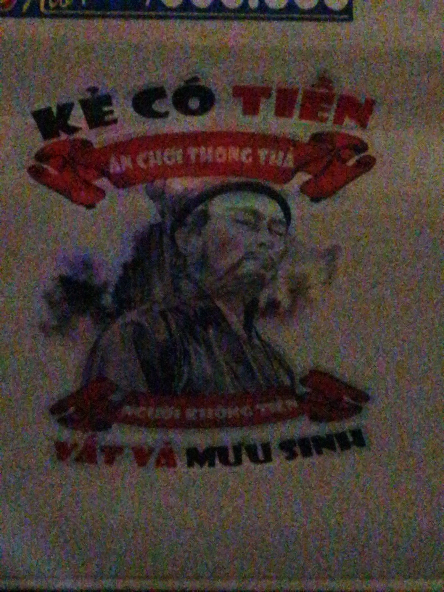 The image shows a close-up of a poster or fabric with Vietnamese text and a drawing. The main subject is a stylized illustration of a person's face and upper body, depicted with dark outlines and muted colors. The person appears to be wearing traditional clothing, possibly a robe and a hat. The facial features are somewhat indistinct due to the image's low resolution and noise.
Several lines of Vietnamese text are visible. The largest text at the top reads "KẺ CÓ TIỀN". Below this, on a red banner shape, is text that appears to say "AN CHƠI THÔNG THU". Further down, another line of text is partially visible, reading "NGƯỜI KHÔNG TIỀN". At the bottom, a larger line of text states "VẬT VÀ MƯU SINH".
The overall aesthetic is somewhat retro or traditional, with a slightly grainy texture to the image. The activity or event taking place is not discernible from the static image itself, but the text suggests themes related to wealth, leisure, and survival. The style of the illustration and the font choices contribute to a sense of cultural context, likely Vietnamese. The setting is not explicitly shown, but the context of the text and imagery points towards a cultural or social commentary. The colors are predominantly dark and earthy tones with pops of red from the banner and some text. The lighting appears to be artificial, illuminating the poster from the front.