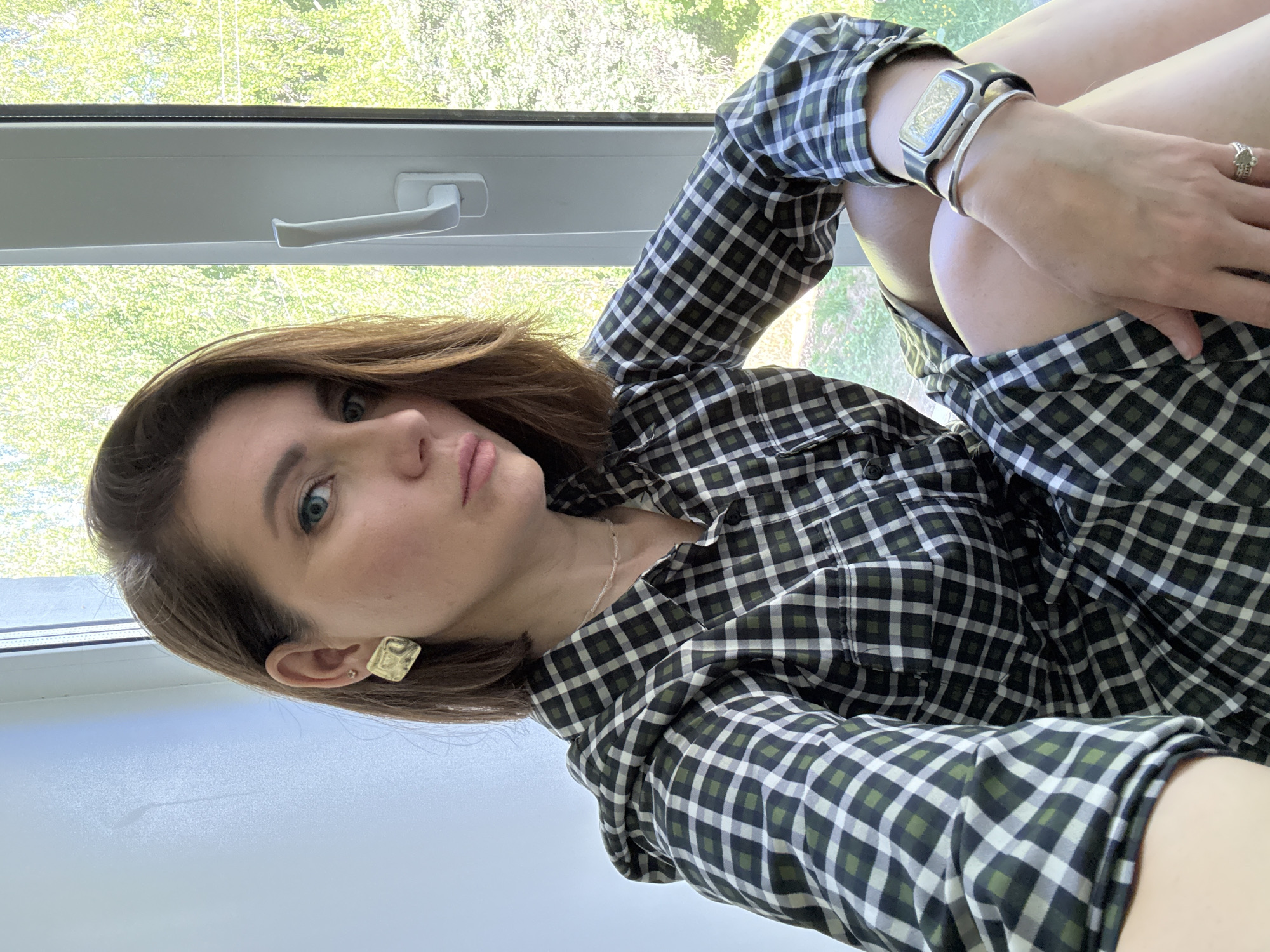 A woman is sitting by a window. She is wearing a black and white checkered shirt, a silver watch and a bracelet. She is also wearing a ring on her right hand and a gold earring on her left ear. The location appears to be in Chaikovsky, Russia, as implied by the user.