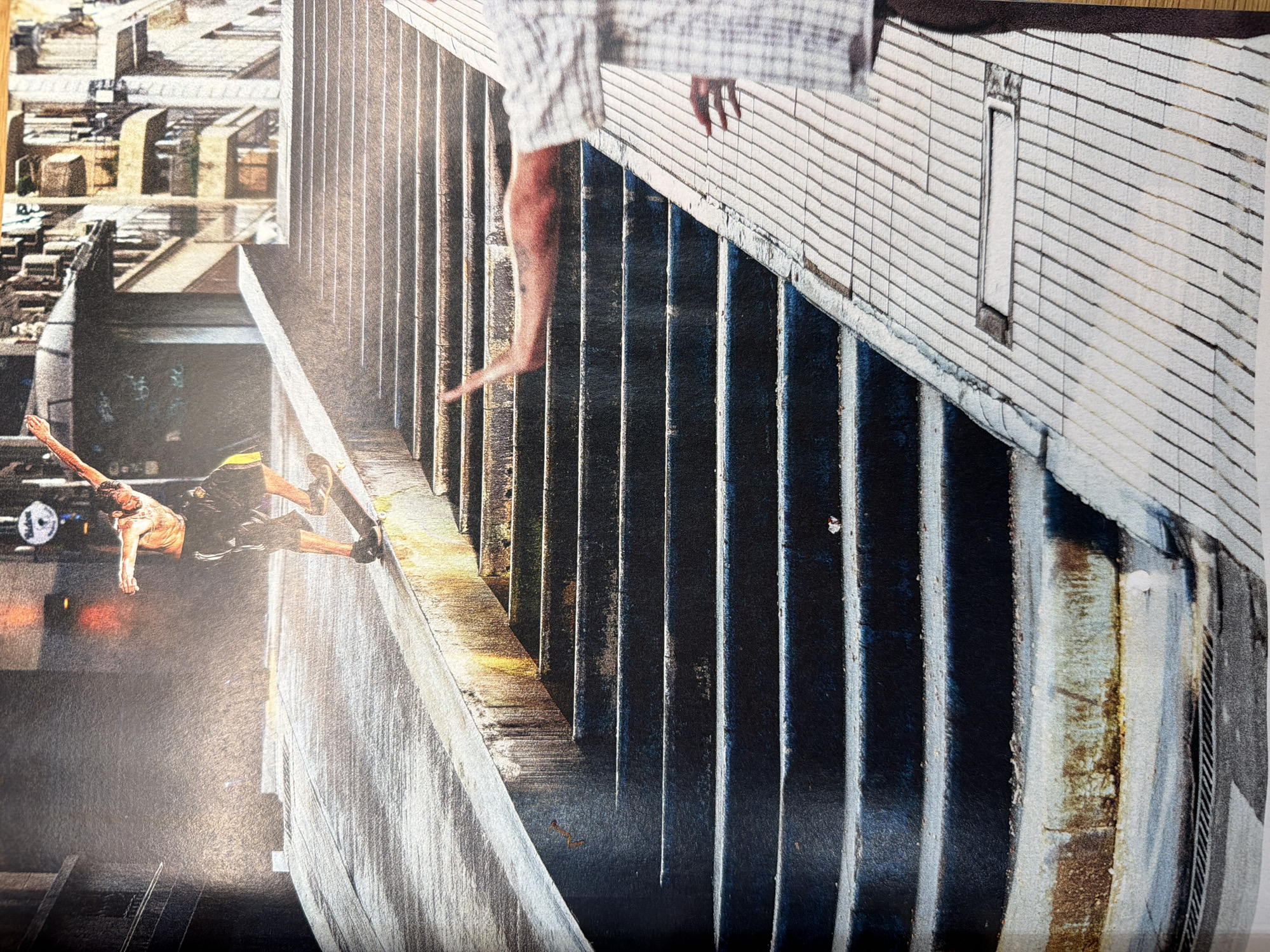 The image depicts a skateboarder in mid-action on a set of stairs. The skateboarder, wearing dark shorts and an orange tank top, is performing a trick on a skateboard, his body angled as he balances. Behind him, a blurred figure with an arm outstretched can be seen on the right side of the frame, also on a sidewalk that runs parallel to the stairs. The environment is urban, characterized by a long, wide staircase with weathered concrete steps and a sloping sidewalk. Buildings with architectural details are visible in the background. The lighting suggests it is daytime, with strong sunlight casting shadows and highlighting the textures of the concrete. The scene appears to be an outdoor urban setting, possibly a public space or park in the city of Lyon, France, given the architectural style.