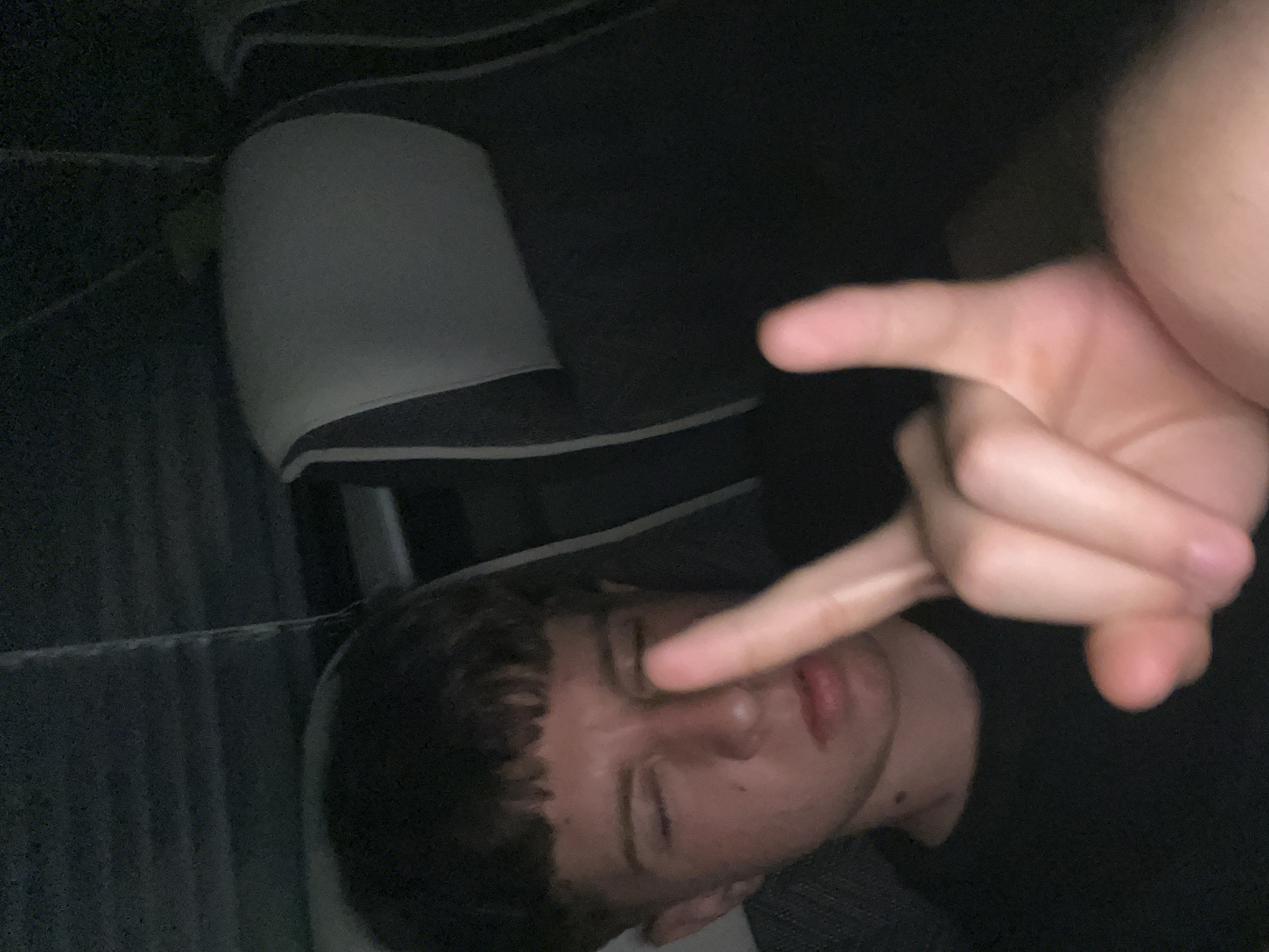 A male is lying down with his eyes closed, with a hand held in front of his face in a gesture. The location is not discernible from the image.