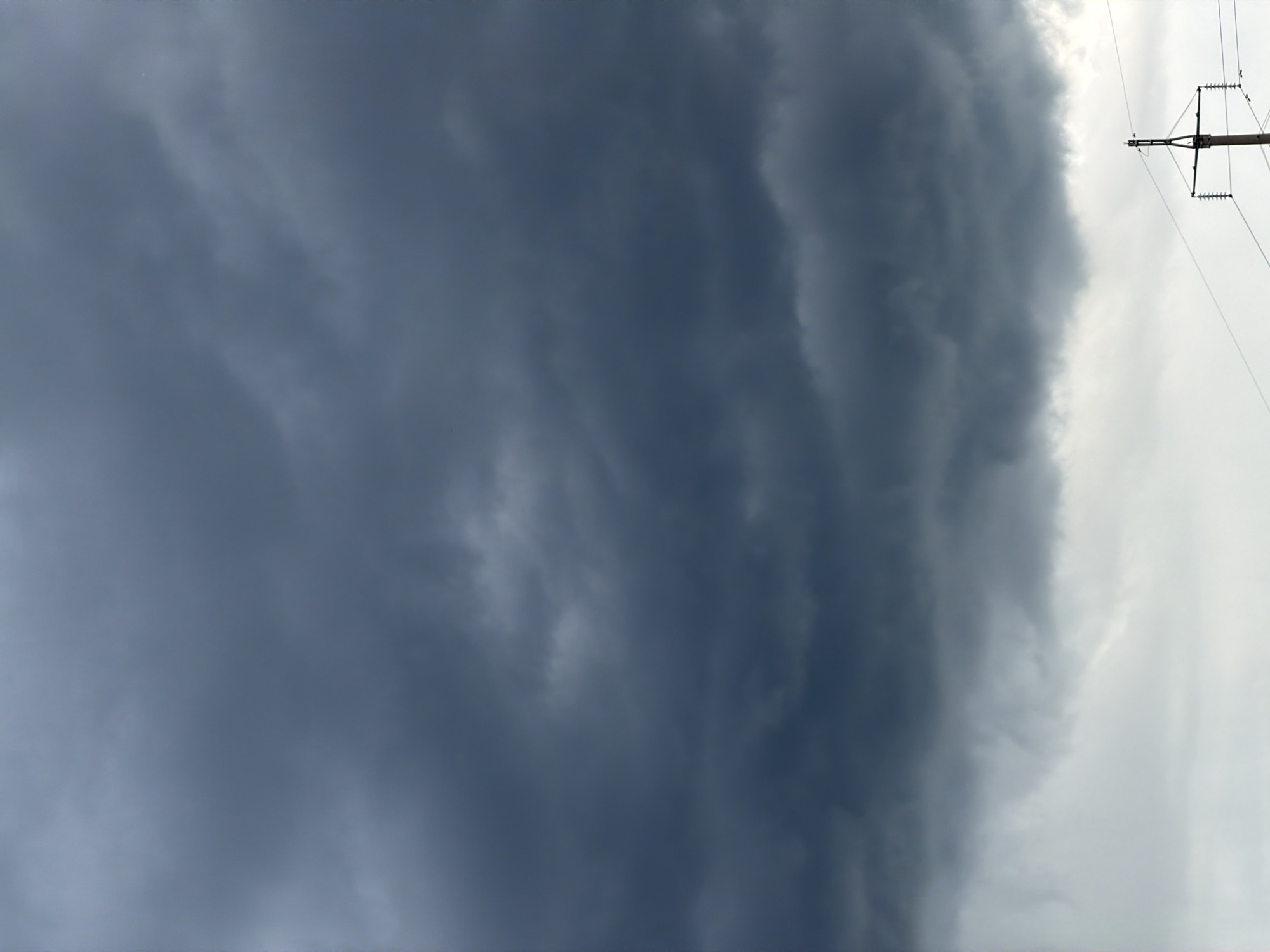The image shows a sky with heavy, dark storm clouds covering a large portion of the frame. To the right, there is a glimpse of lighter sky and a power line support structure with wires extending outwards. The location is speculated to be in the city of Chaikovsky, Russia, but without further visual or contextual evidence, confirmation is not possible. There are no people or other identifiable objects in the frame besides the clouds and power lines.
