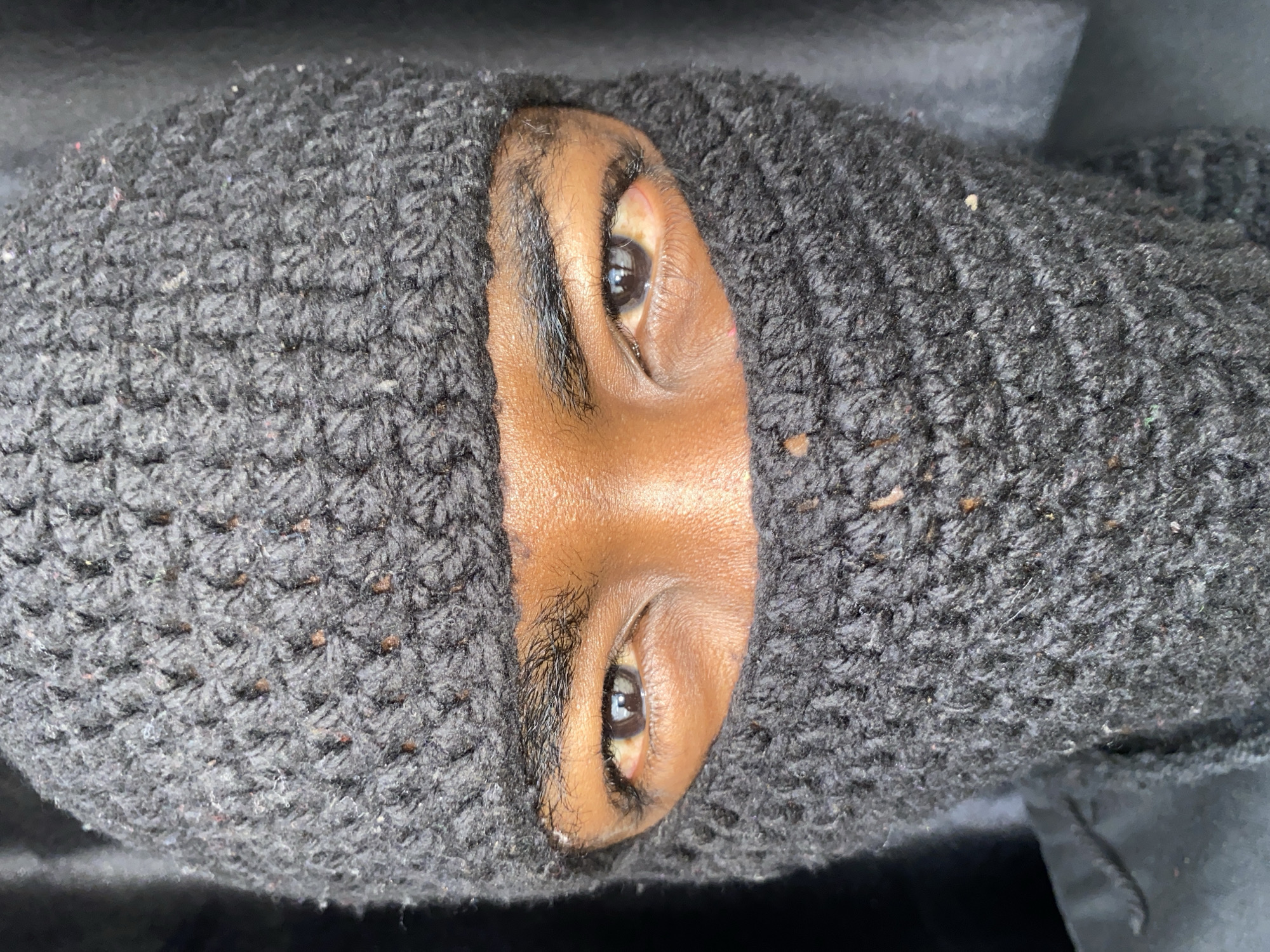 A close-up, straight-on shot depicts a person wearing a dark gray knit balaclava that covers most of their face, leaving only the nose and eyes visible. The person's skin is brown. The background is indistinct and dark. The location, Barakin Akawo, Nigeria, cannot be confirmed from this image.