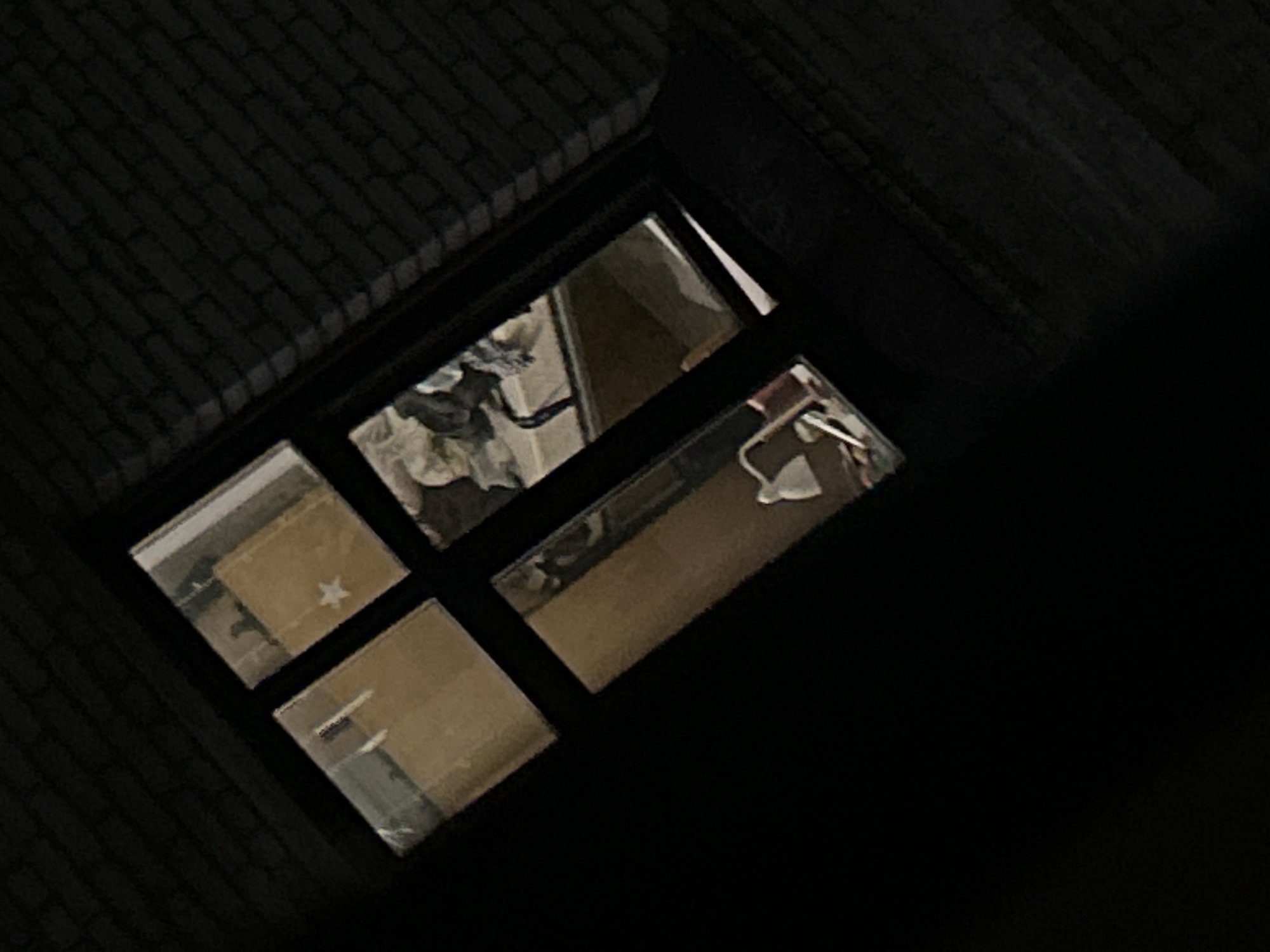 The image shows a partially opened, rectangular container on a dark surface that appears to be made of a brick-like pattern. Inside the container are four compartments containing reflective surfaces or mirrors. The reflections show a cluttered room interior, including clothing, furniture, and possibly a sink fixture. The image is very dark and lacks strong definition, so a precise location and further details are difficult to ascertain. The location is Unknown, Unknown.