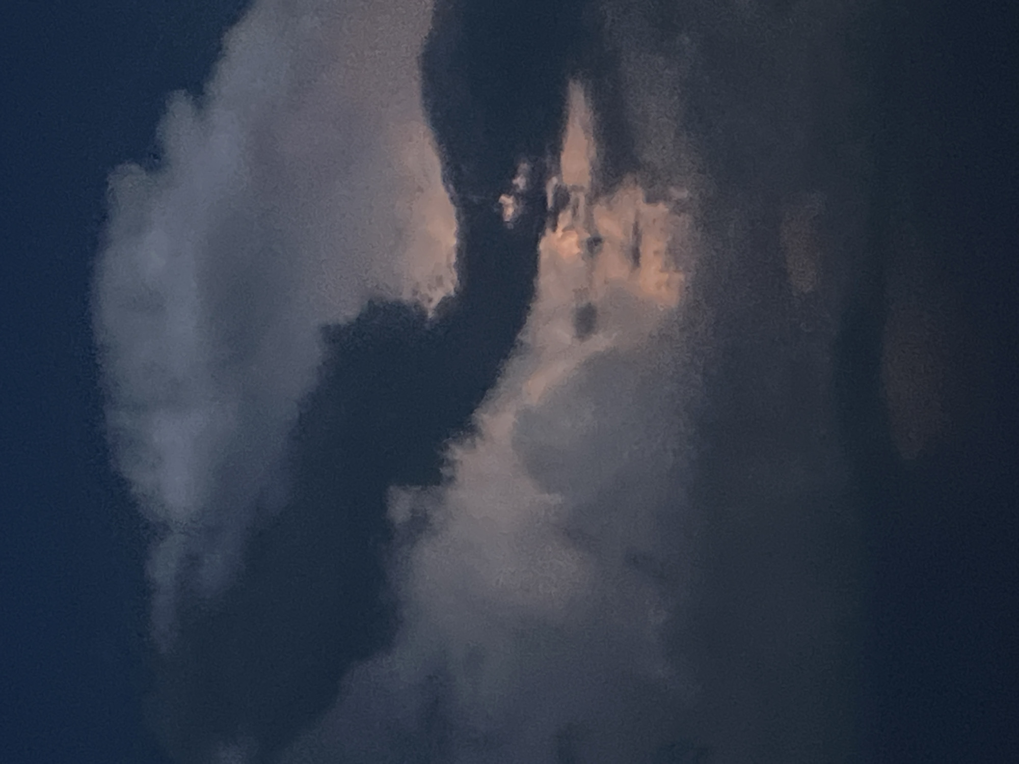 The image shows a dark sky filled with dramatic, layered clouds. The clouds are a mix of deep grays and blues, with some areas catching a faint, warm light, suggesting either sunset or sunrise. The lighting creates a sense of depth and texture within the cloud formations. There are no visible structures, people, or other discernible objects within the frame, making it a purely atmospheric image of the sky. The location in Novopichugovo, Russia, is inferred and not visually depicted in the image itself.