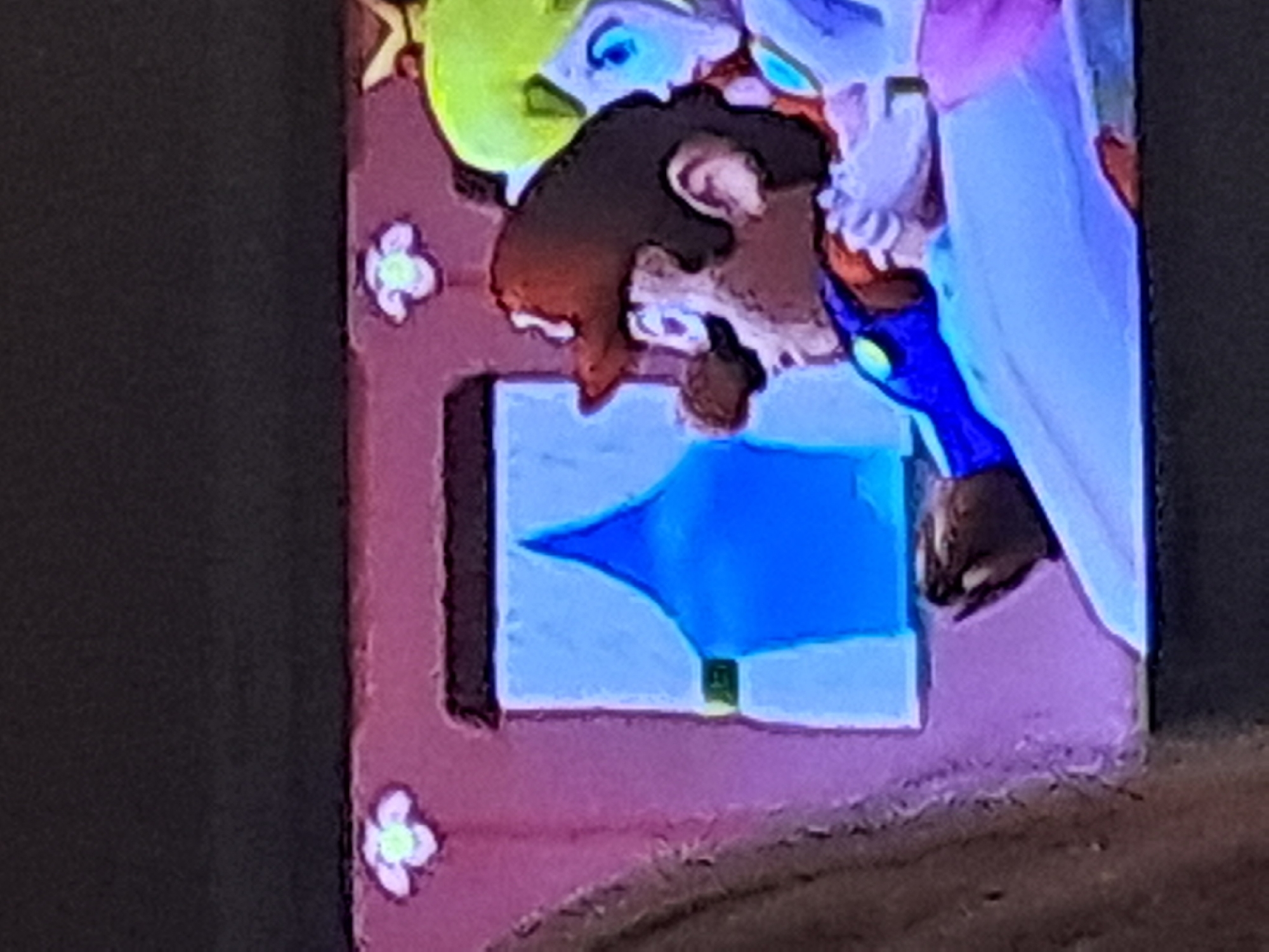 The image shows a close-up of a screen displaying a scene from a video game, likely Super Mario Odyssey. In the foreground, a character resembling Mario is depicted in profile, wearing his signature red cap and blue overalls. He appears to be holding something with his right hand. To his right, partially visible, is a character resembling Princess Peach with blonde hair. They are both seated inside what appears to be a carriage or vehicle, indicated by a pink interior with decorative floral elements and a window with a blue curtain. The overall aesthetic is illustrative and cartoonish, typical of video game graphics. The scene is set against a dark background that could represent the sky or the exterior of the vehicle. There is no discernible information about the location within a city as this is a digital rendering.