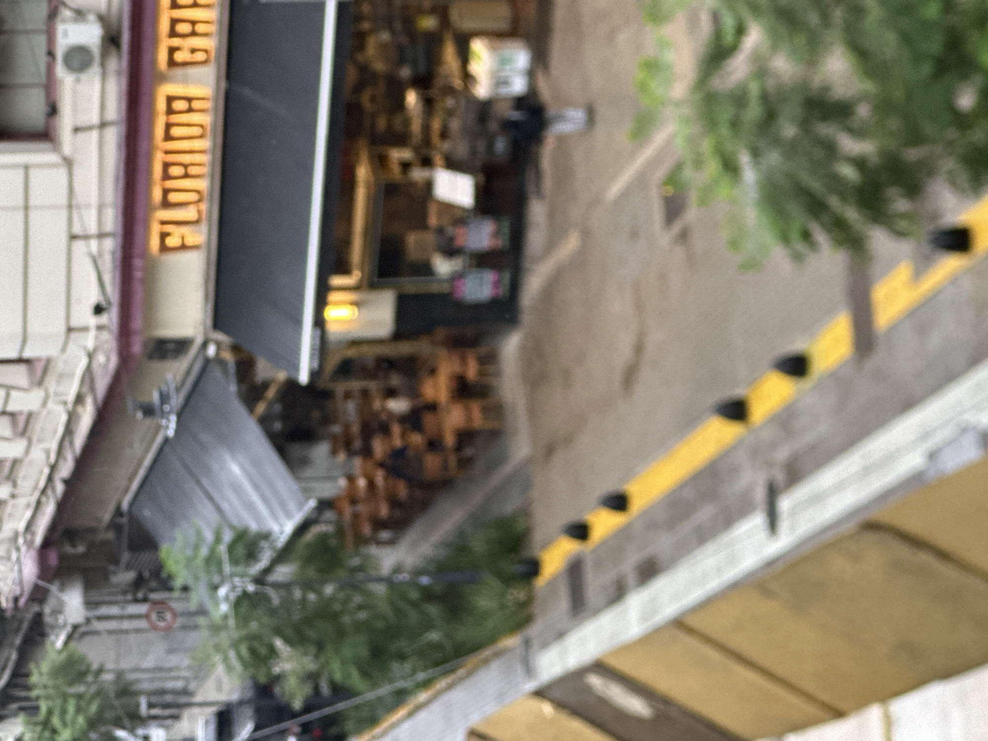 The image depicts a street scene featuring a restaurant called "Florida Cafe" in Buenos Aires, Argentina. The sign of the restaurant is illuminated and prominently displayed. Tables and chairs are visible inside the restaurant. Outside, there are trees and a barrier with yellow and black markings along the sidewalk. A person is seen walking on the street.