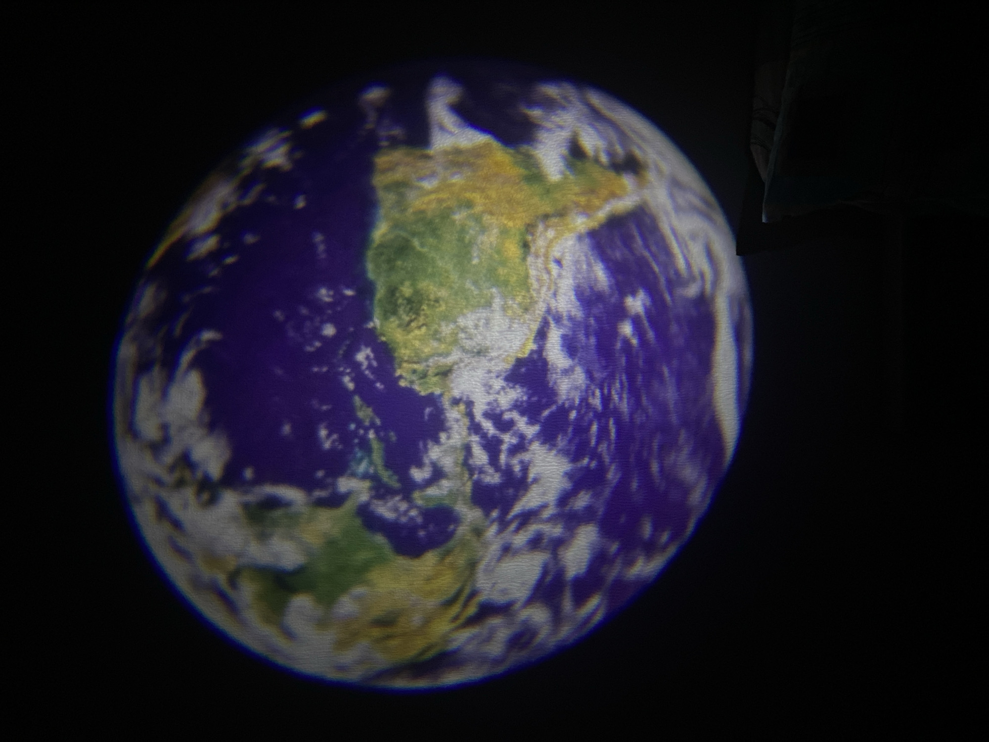 A blurry image of the Earth is centered in the frame against a black background. The landmasses of North and South America are visible. The image is likely from a projector or screen. There is no indication of the location being Saint Petersburg, Russia, or any people or actions.