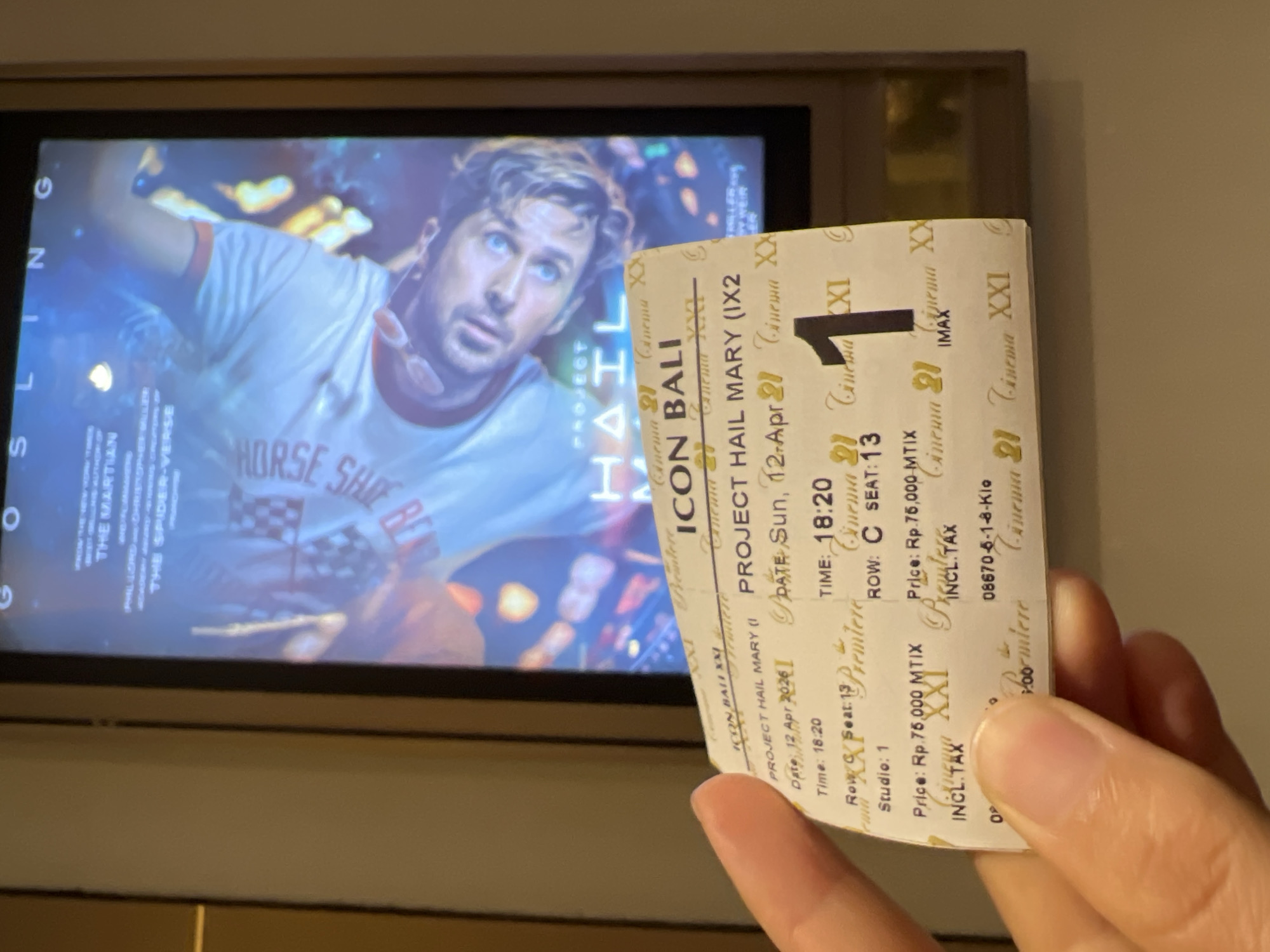 A hand holds a Cinema XXI ticket in front of a screen displaying the movie "Project Hail Mary". The ticket indicates the location as Icon Bali, showing on Sunday, April 12, 2026, at 18:20 (6:20 PM), seat C13. The price is Rp. 76,000. Cinema XXI is a cinema chain in Indonesia with locations in multiple cities, including Denpasar.