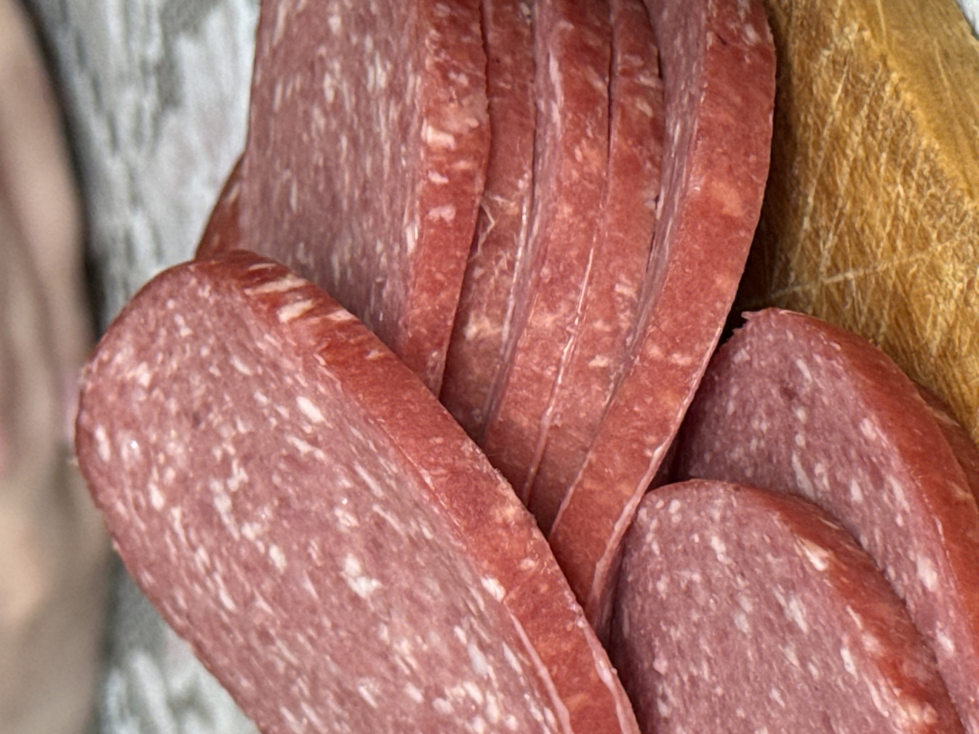 The image shows a close-up of sliced salami. The slices are arranged in a pile, with some overlapping. The texture of the salami is visible, including the marbled pattern of meat and fat. A wooden surface is visible in the background. Верхнеказымский, Russia is irrelevant to the image content.