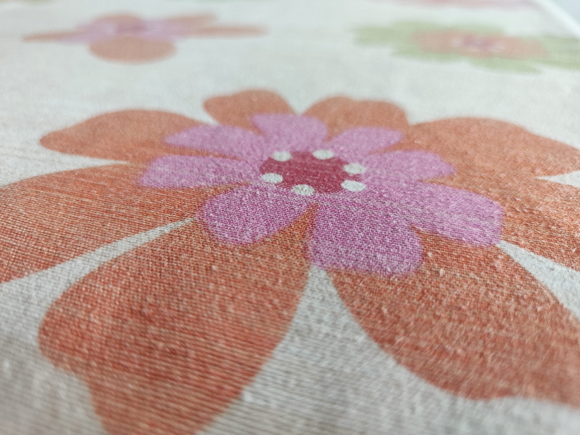 The image shows a close-up view of a fabric with a floral pattern. The flowers have large petals in shades of pink and orange, with white dots in the center. The fabric appears to be textured and slightly fuzzy. The image does not contain any information about the city of Voronezh, Russia, or any people, actions, or interactions. It is a still life image focused solely on the textile design.