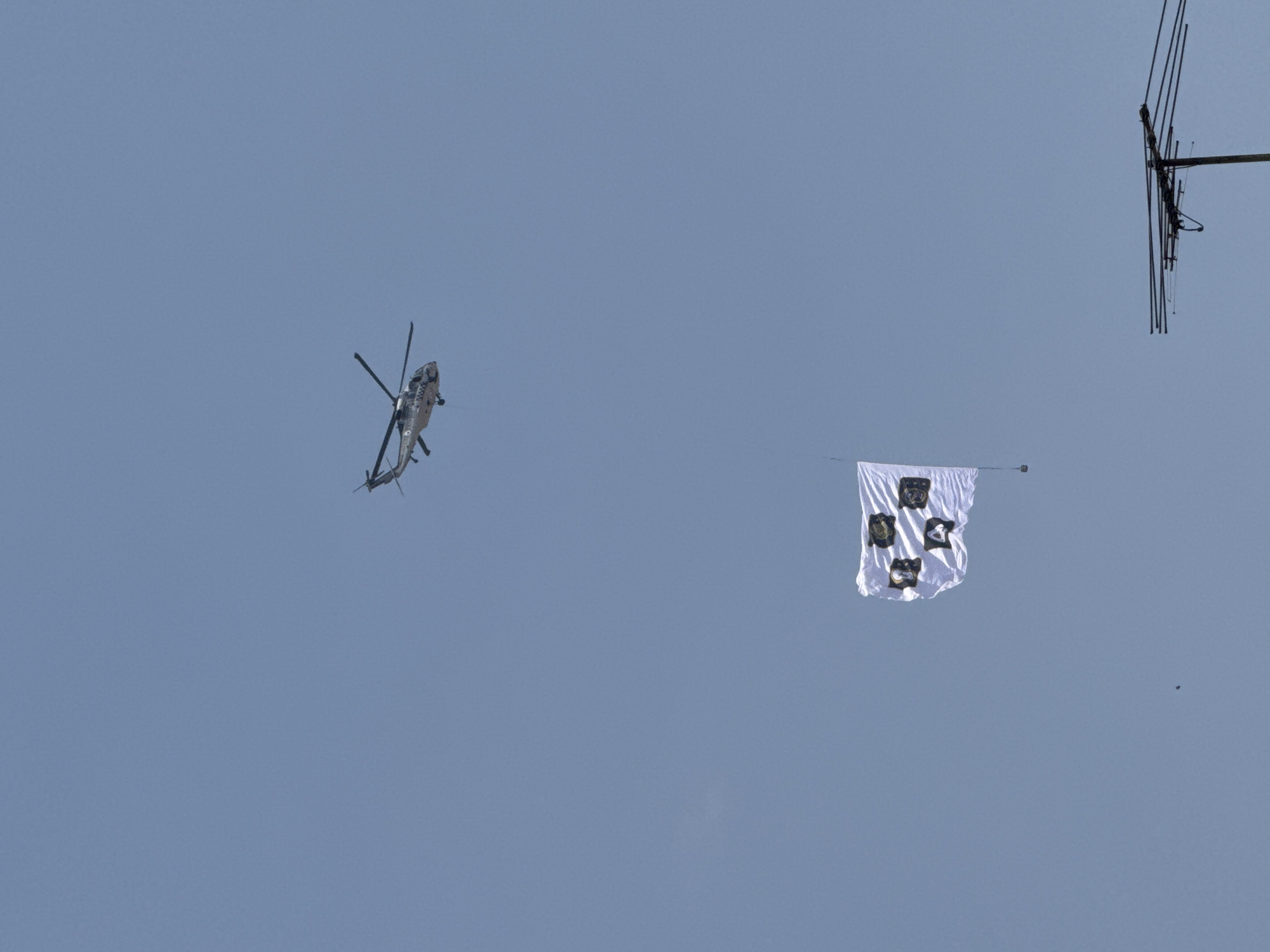 A helicopter flies in the light blue sky near a white flag with black images attached to the side and an antenna in the upper right side of the frame. The location is the city of Puebla, Mexico.