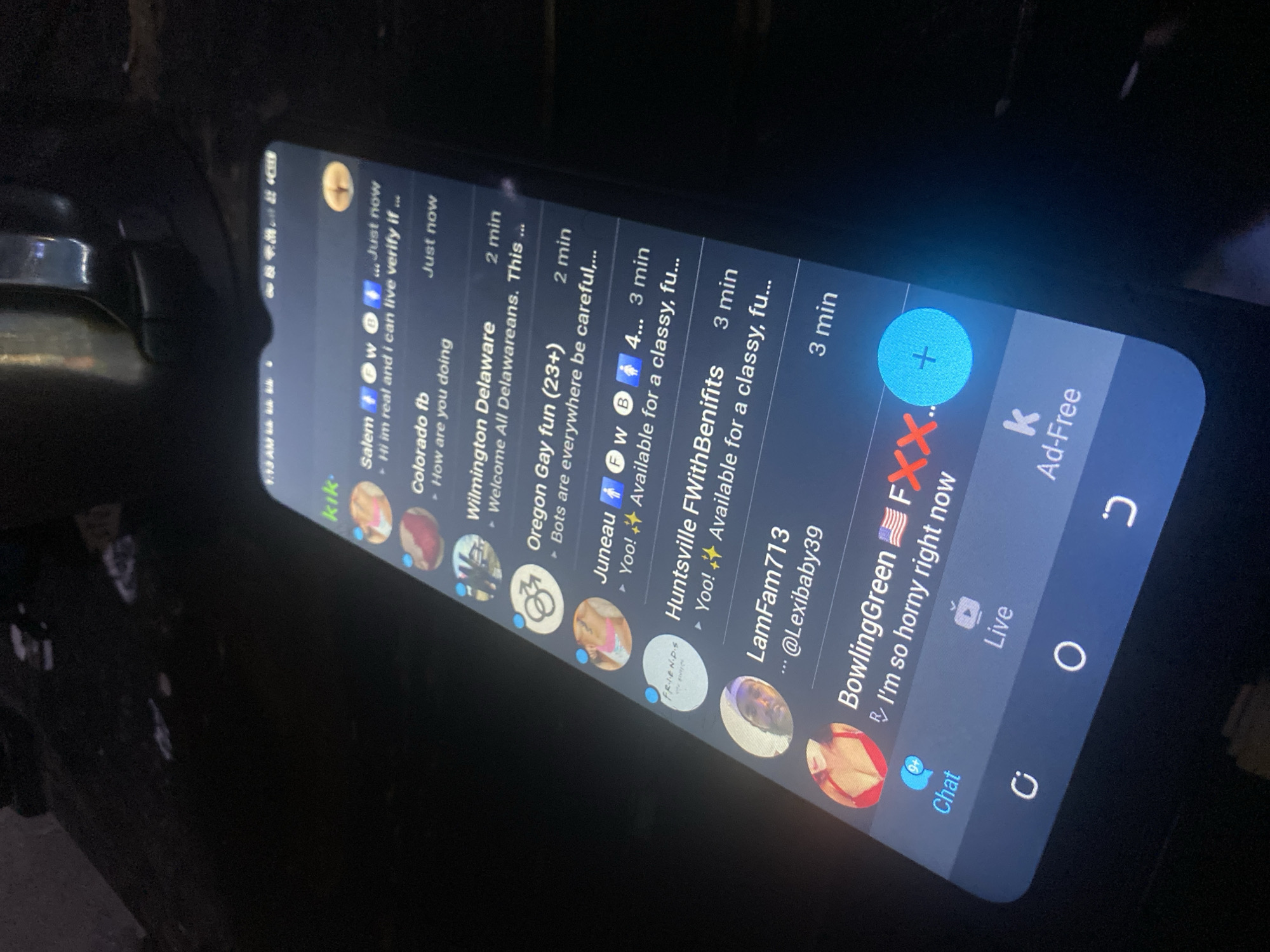 A close-up image shows a black smartphone displaying the Kik messaging application. The screen shows a list of chats, including titles such as "Salem," "Colorado fb," "Wilmington Delaware," "Oregon Gay fun (23+)," "Juneau," "Huntsville FWithBenifits," "LamFam713," and "BowlingGreen," along with timestamps. The app's bottom navigation bar features icons for "Chat" and "Live," as well as an "Ad-Free" indication. There is no evidence that this photo was taken in the city of Bukuru, Nigeria, or any information about people or actions.