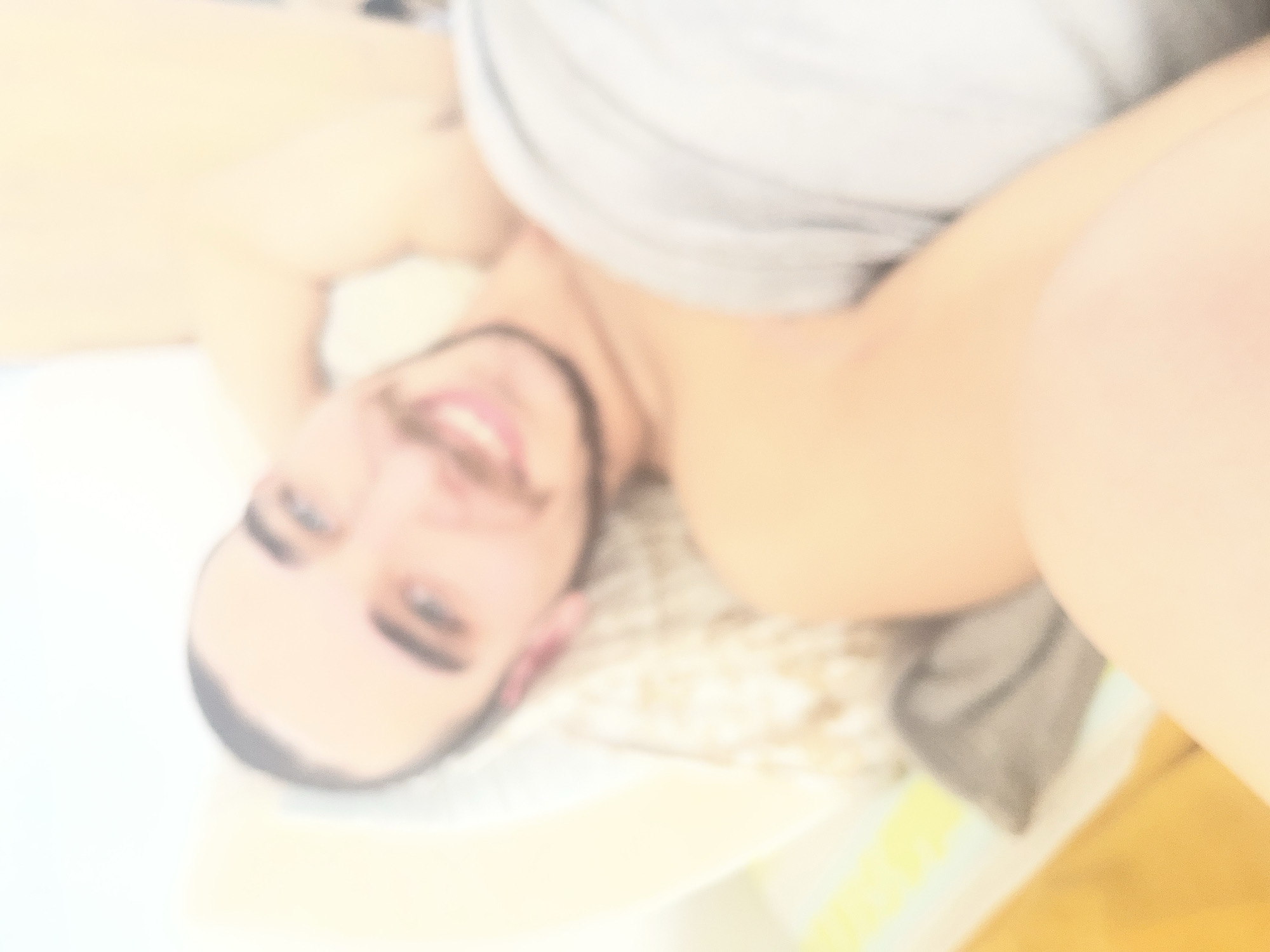 A blurred image of a man lying on his back on a bed. He has a beard and short dark hair. He is wearing a light gray shirt. The background is out of focus, but includes a white surface and a patterned cushion or sheet. No landmarks indicate the location in Varna, Bulgaria.