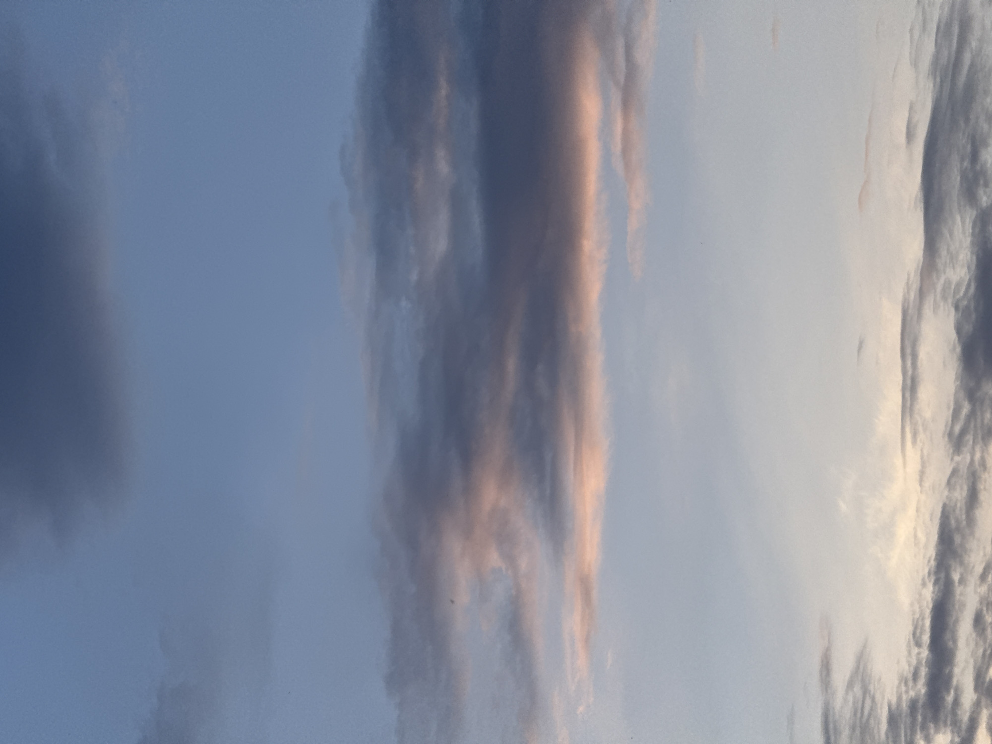 The image shows a sky with various types of clouds. Some clouds are dark and dense, while others are lighter and more wispy. The clouds appear to be vertically oriented in the frame, suggesting a specific atmospheric condition. The sky's color ranges from light blue to white. There are no identifiable people, subjects, objects, actions, or interactions within the frame. The location in the city of Sarapul, Russia cannot be determined from the image.