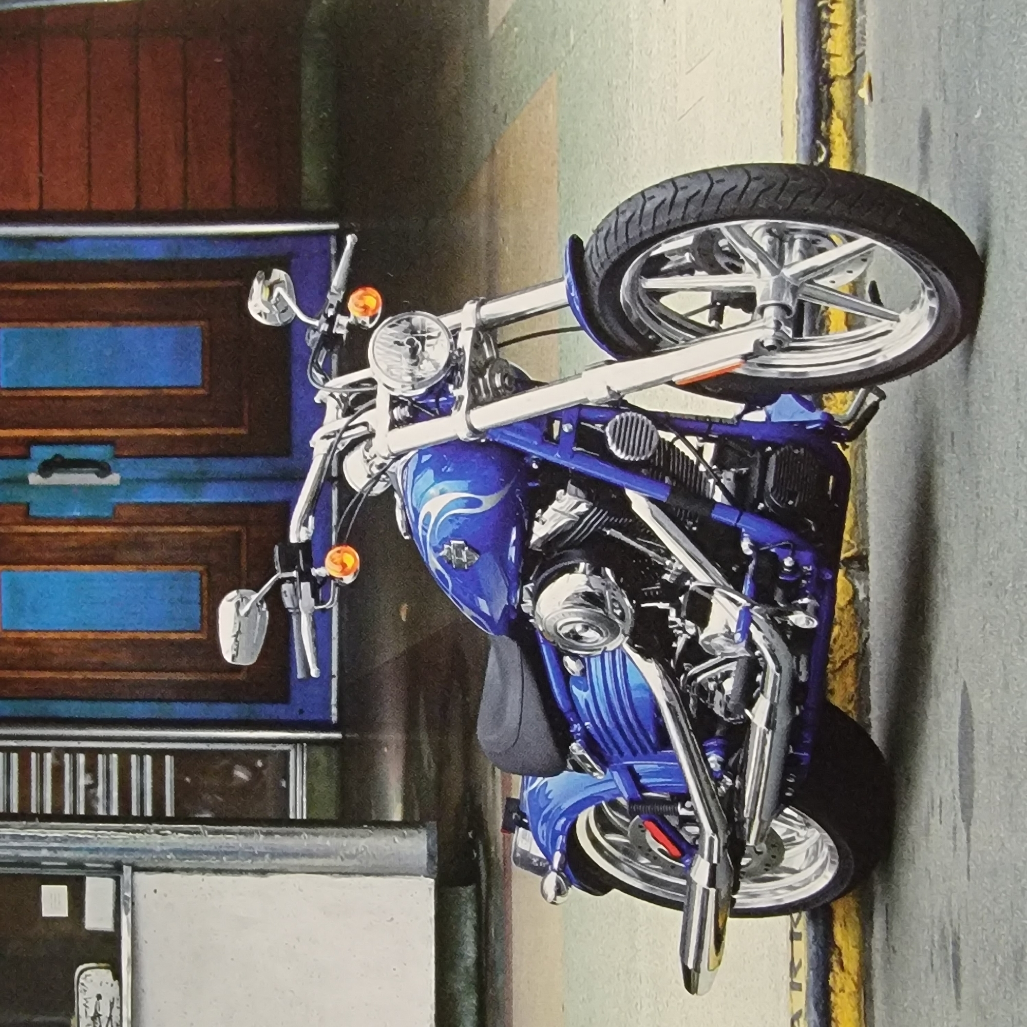 This media file features a close-up, angled shot of a vibrantly colored blue motorcycle, likely a custom chopper, parked outdoors. The motorcycle is the central focus, showcasing its polished chrome parts, intricate engine details, and a flame graphic on the fuel tank. Its large, spoked front wheel and thick tire are prominently displayed.
The motorcycle is positioned alongside a building with a dark red, paneled facade and blue rectangular accents. Further to the right, a yellow and black striped line, possibly a curb marking or a bollard, runs along the edge of a textured gray surface that appears to be asphalt or concrete. The overall lighting suggests it is daytime, and the scene appears to be a street or an alleyway, offering no specific clues about the time of day or weather conditions. The image is static, with no discernible activity or event taking place other than the motorcycle being parked. There is no visible text within the frame.