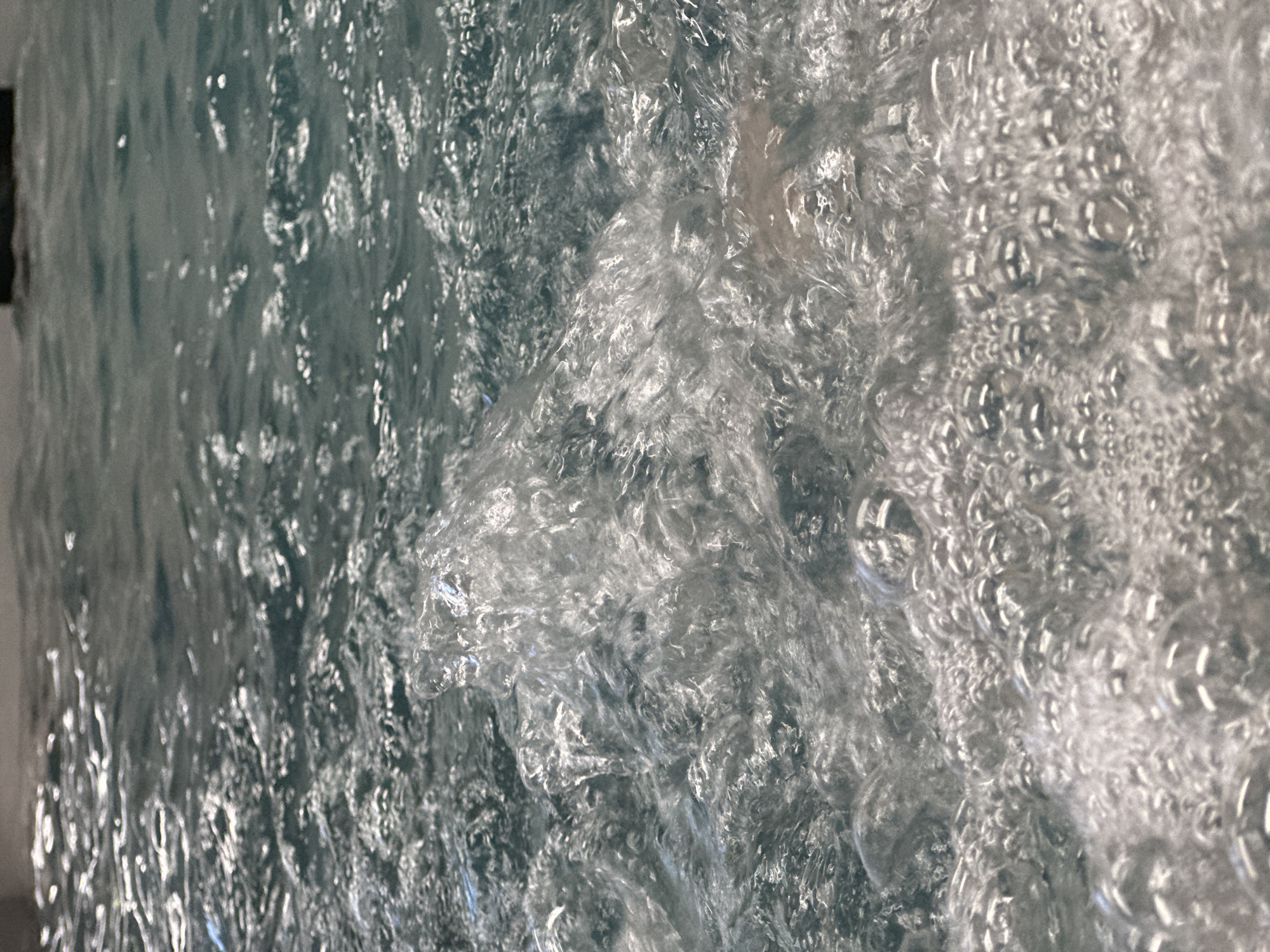The image shows turbulent, bubbly water. It is unclear whether the location is in the city of Chaikovsky, Russia. There are no people or identifiable objects. The scene is a close-up of water with many bubbles. The water appears to be agitated or aerated.