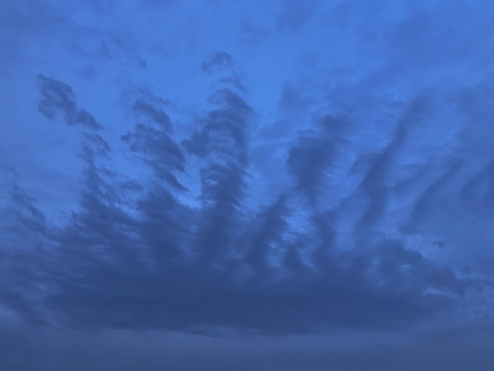 The image shows a stormy sky with dark blue and grey clouds in Taldykorgan, Kazakhstan. The clouds are heavy and textured, with some appearing to be in waves or streaks. The lighting is dim, suggesting it is either dawn, dusk, or overcast. No people, subjects, objects, or actions are visible in the image; only the sky and clouds are depicted. The environment is exclusively the sky.