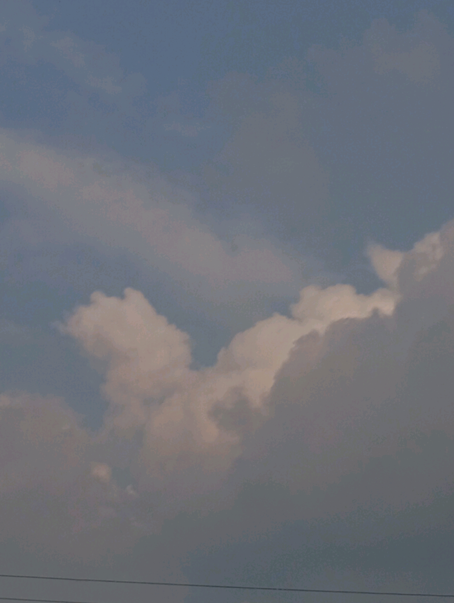 A cloudy sky with light and dark gray clouds. The clouds are lit by a warm light from below. There are also some thin, wispy clouds. There are two thin horizontal lines in the bottom of the image, which are likely power lines. The location is Cimahi, Indonesia.
